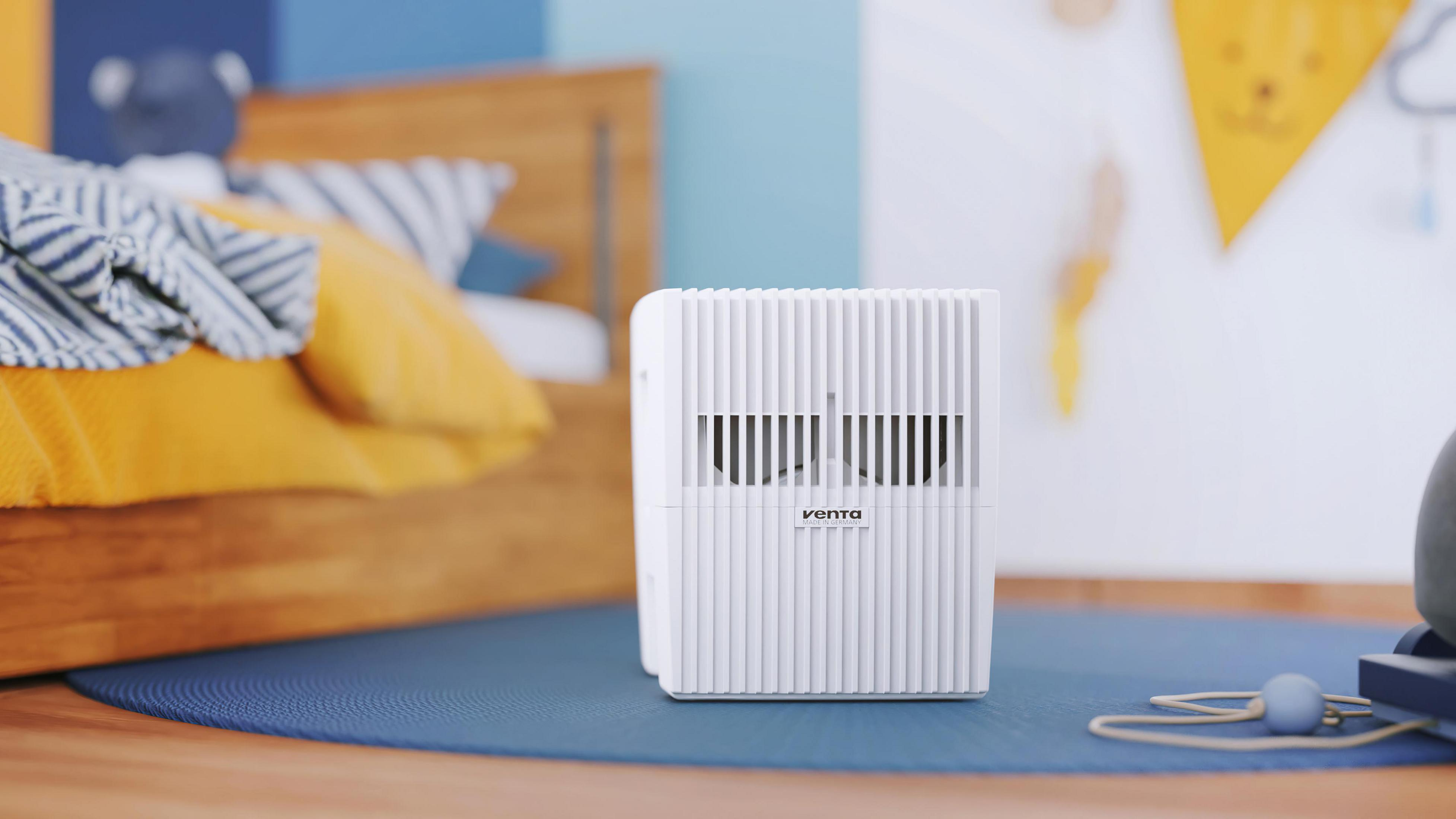 Purificatore d'aria bianco nella cameretta di un bambino. Sono visibili un letto, dei giocattoli e un tappeto blu.