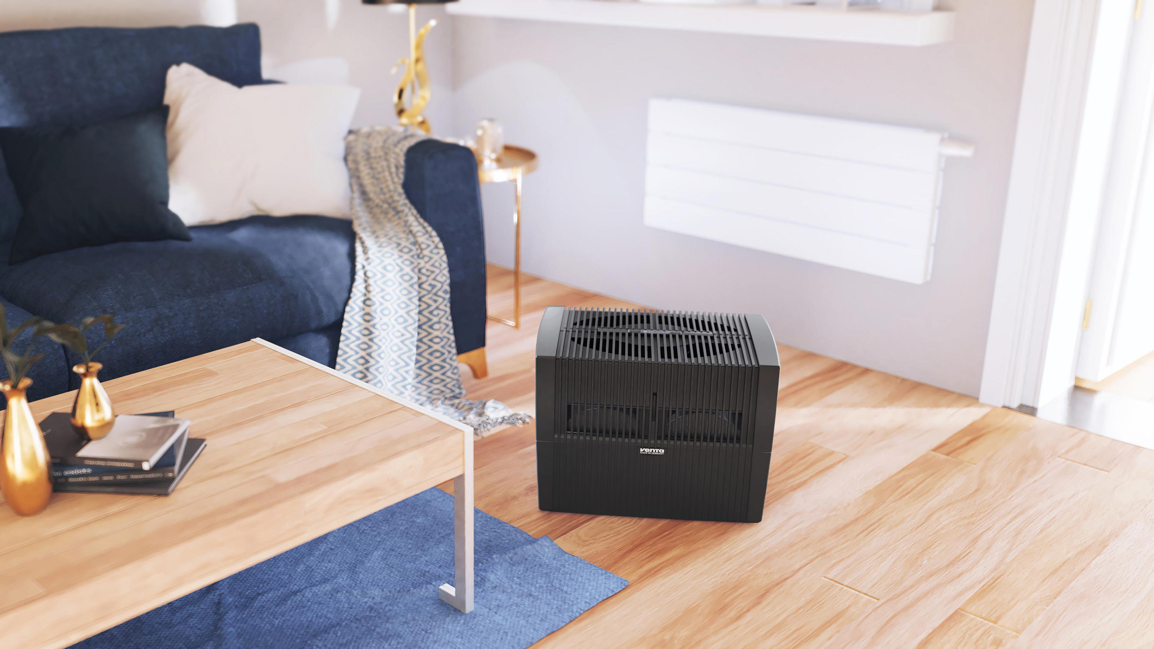 A living room with a couch, coffee table, a black humidifier, and a wall heater.