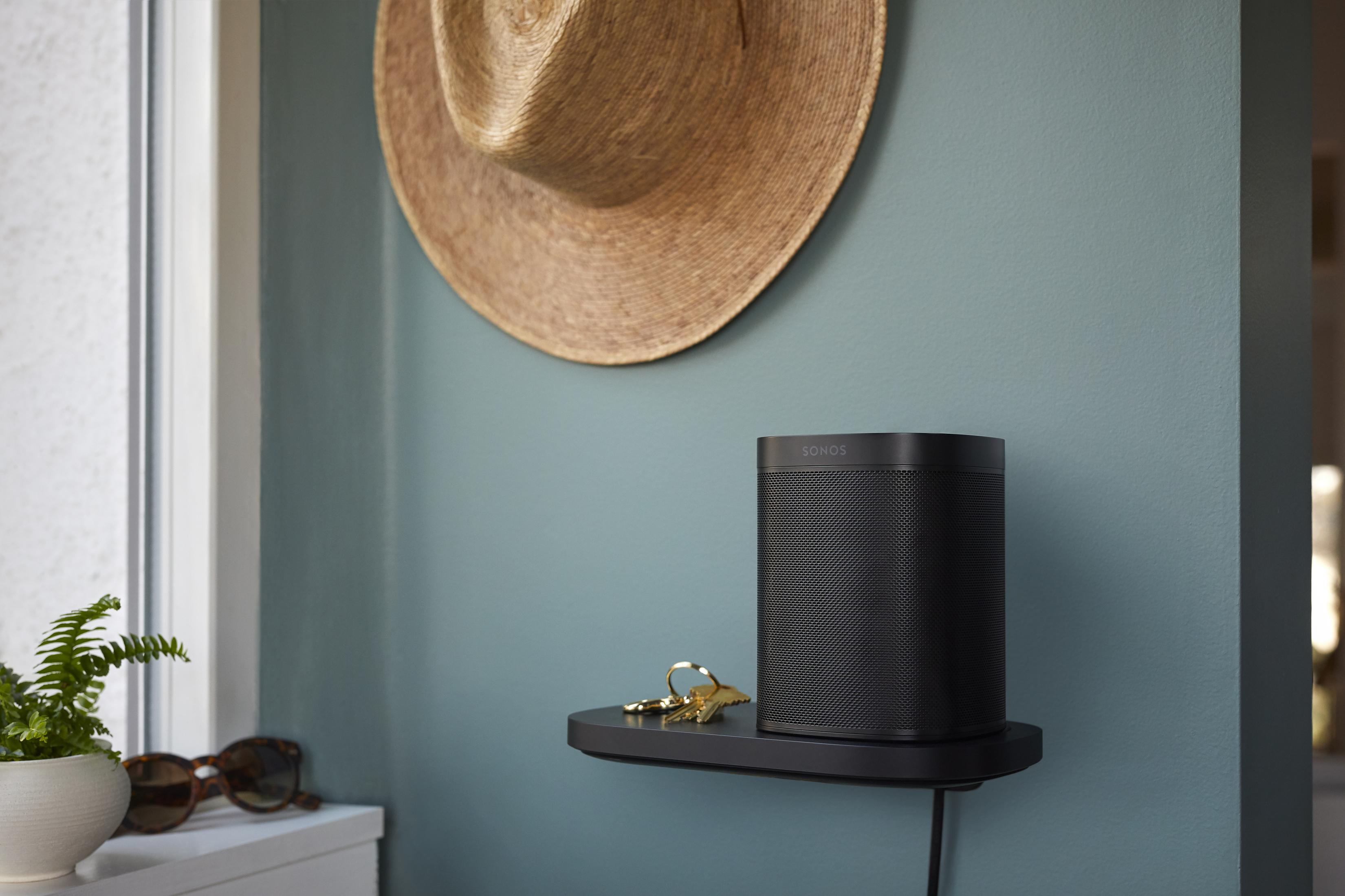 Altavoz negro en un estante, sombrero y accesorios, junto a una pared.