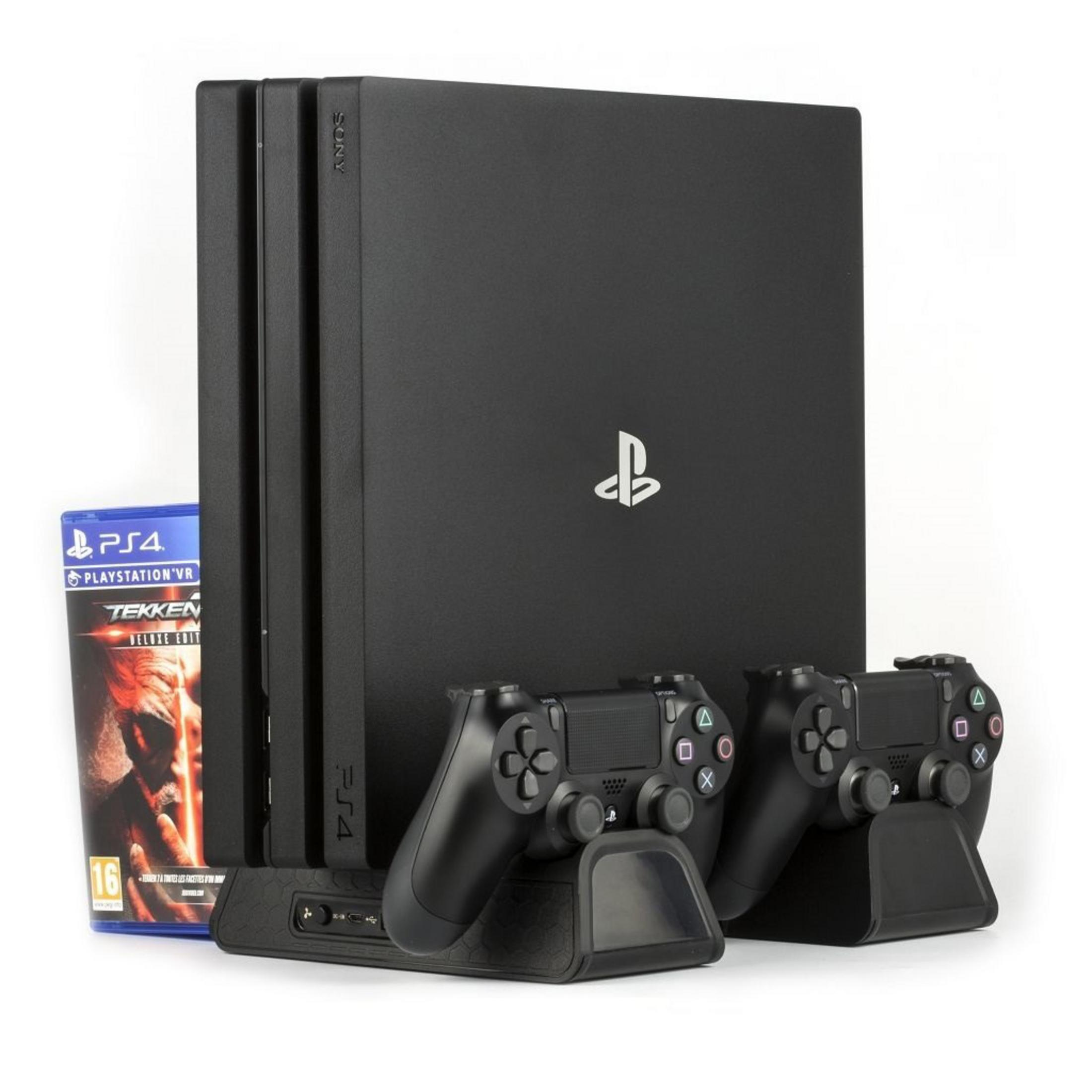Czarna konsola PS4, dwa kontrolery, pudełko z grą (Tekken) i stacja ładująca.
