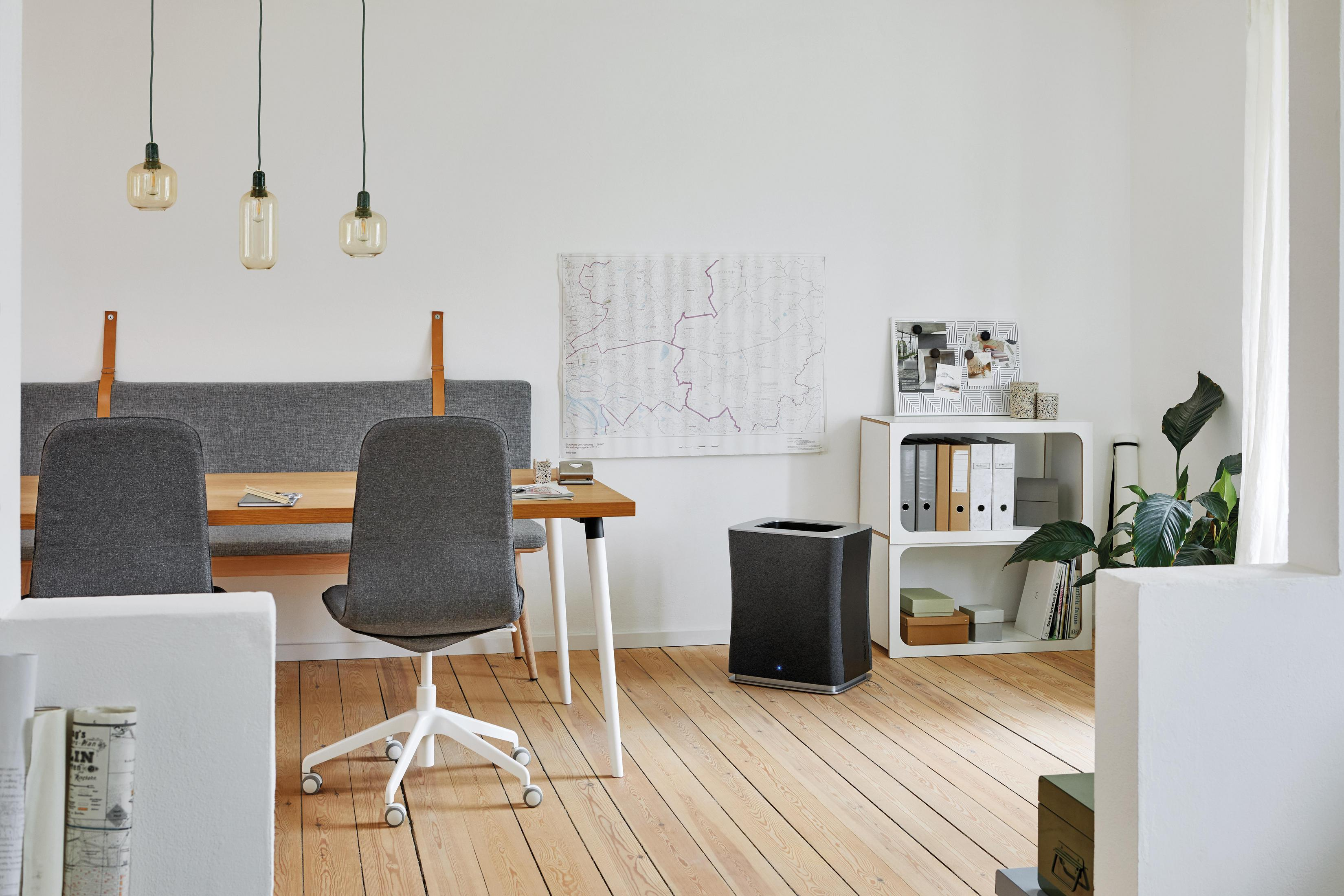 Office interior with a table, chairs, and an air purifier. Map on wall, lights hanging, and wooden floors.