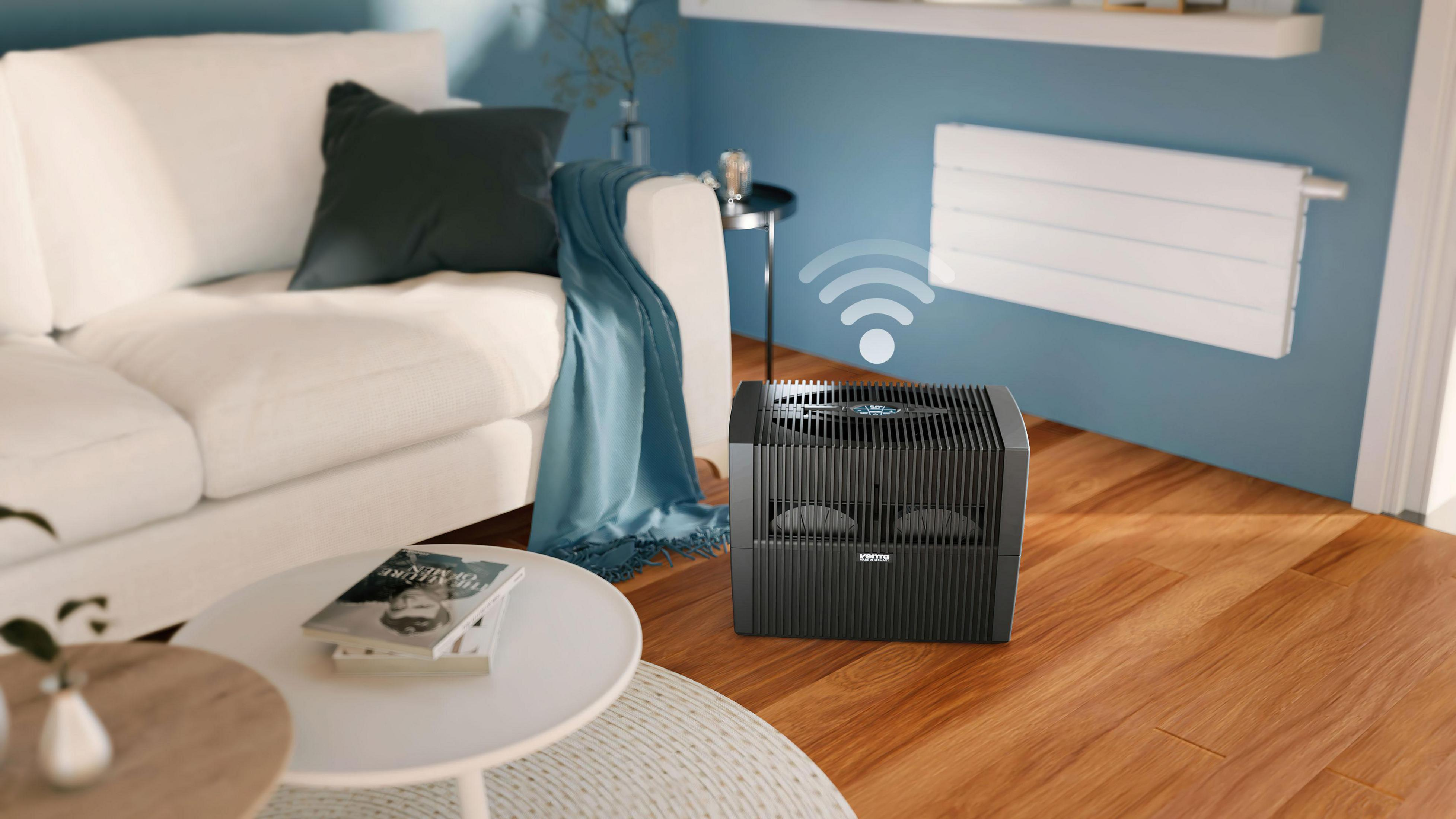 Scena w salonie. Czarny nawilżacz na drewnianej podłodze, biała kanapa i niebieskie ściany są widoczne.