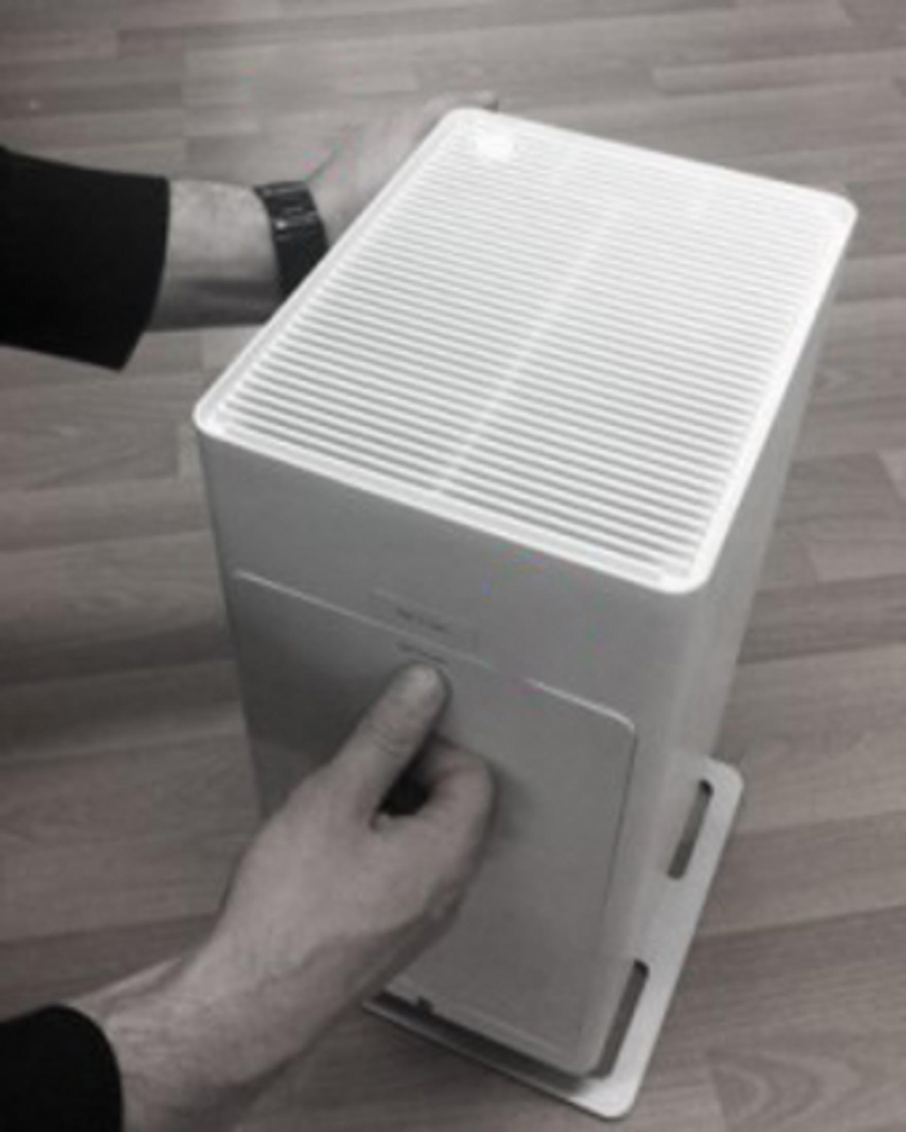 Hands assembling a white air purifier. Gray wooden floor. White background, monochrome.