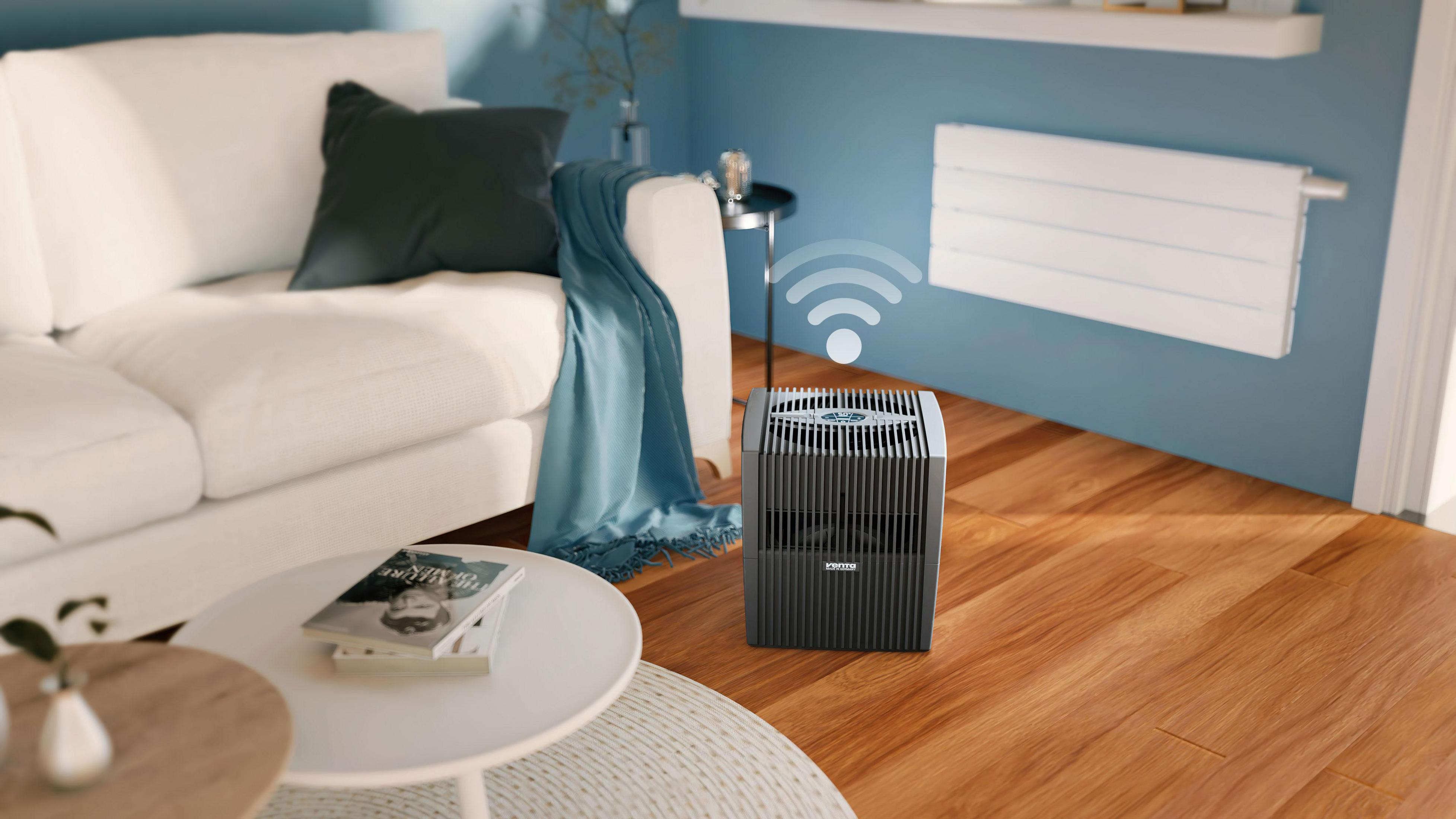 Scena w salonie z białą sofą, drewnianą podłogą i oczyszczaczem powietrza. Widoczny symbol Wi-Fi.