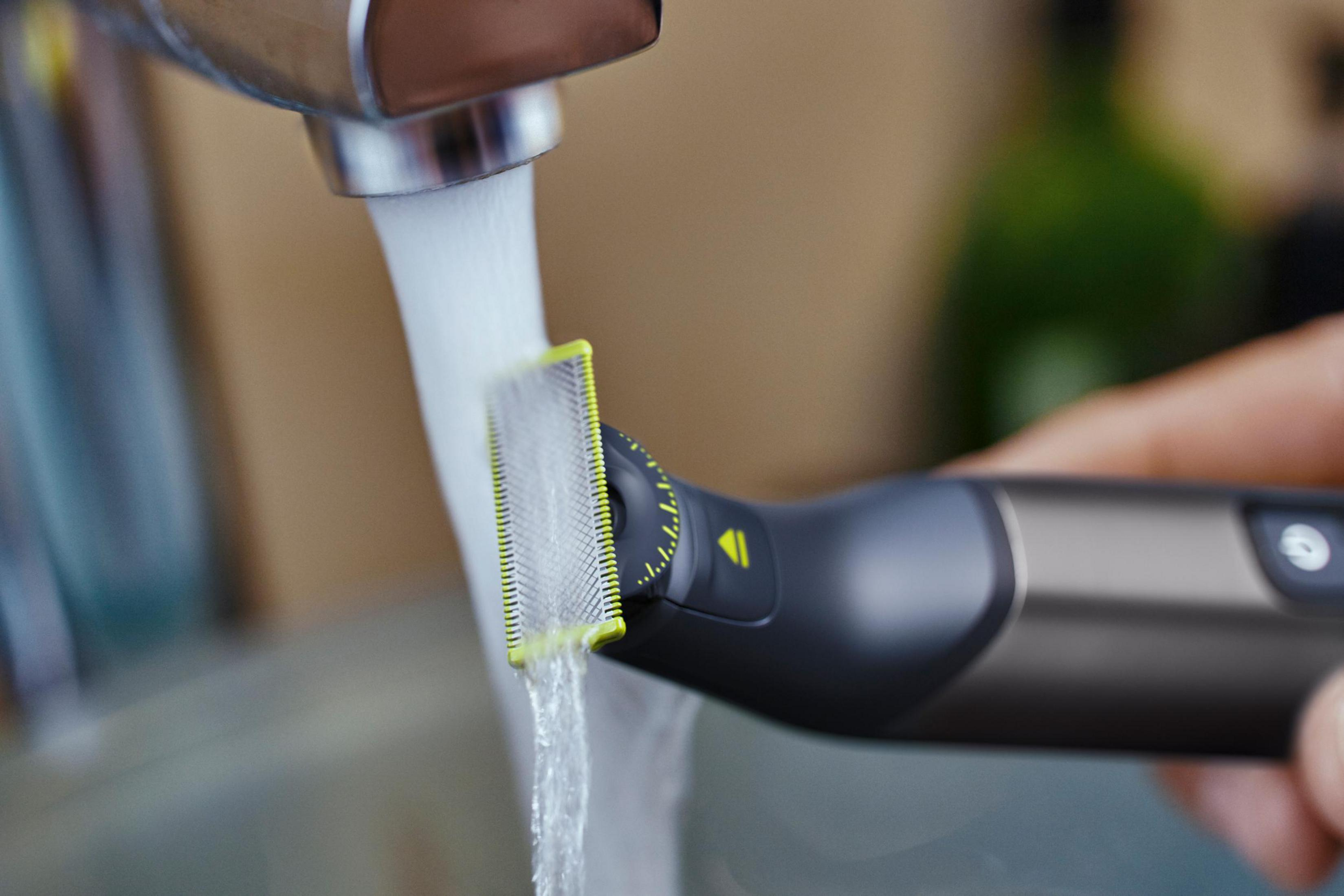 Czarna i szara golarka elektryczna pod bieżącą wodą. Woda spływa po ostrzu.