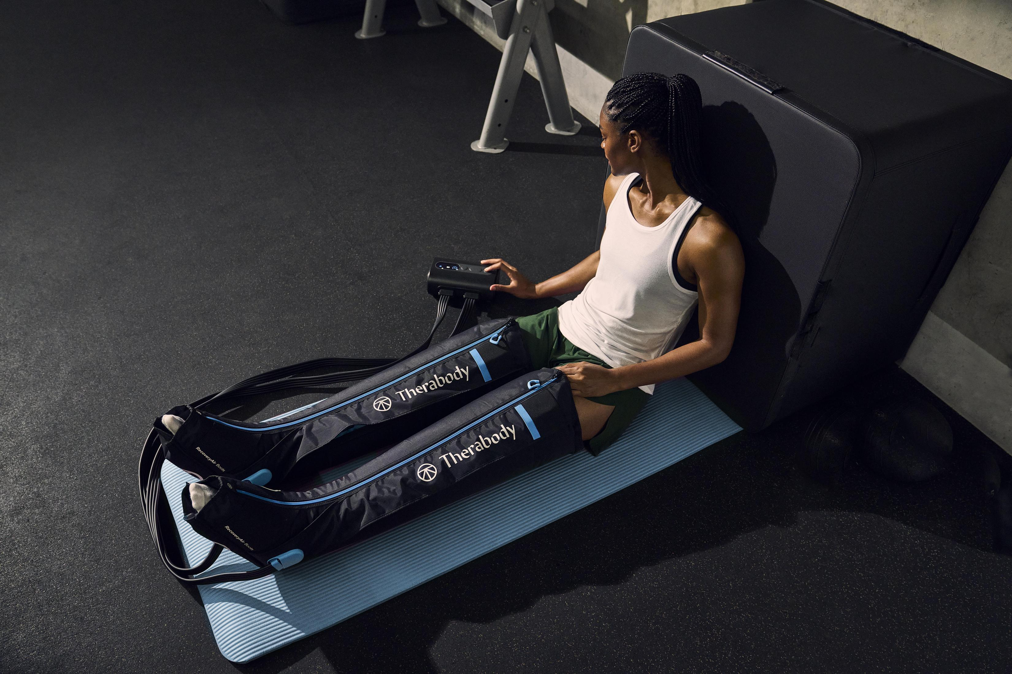 Frau, die eine Bein-Kompressions-Therapie auf einer blauen Matte in einem Fitnessstudio anwendet.
