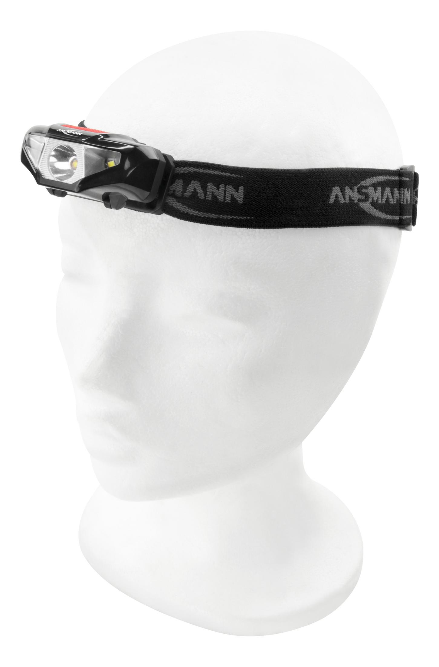 Latarka czołowa na głowie manekina. Czarny pasek z białym tekstem. Światło włączone i czerwony akcent.