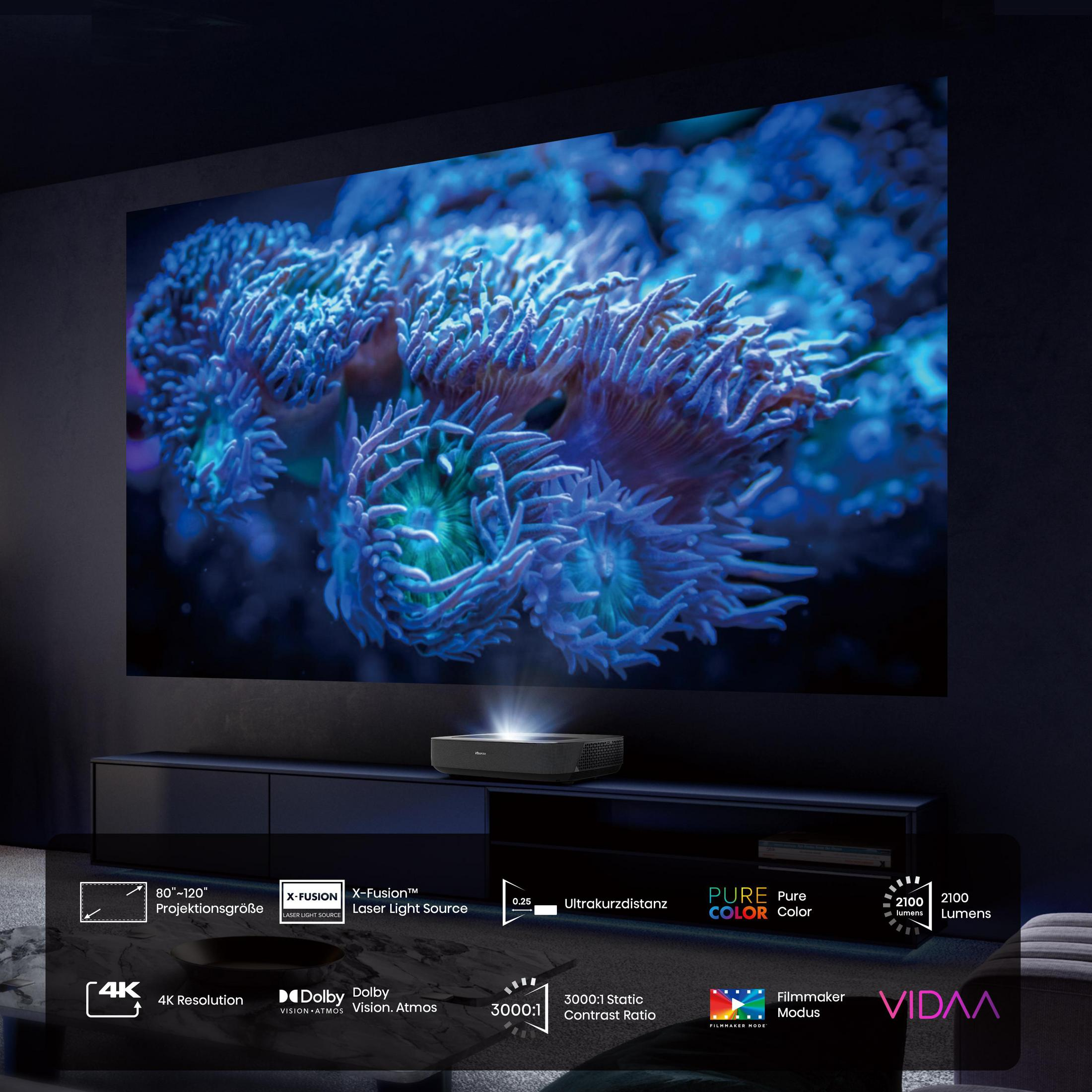 Projektor na czarnej powierzchni, wyświetlający żywy niebieski obraz na dużym ekranie. Tekst: 4K, Dolby.