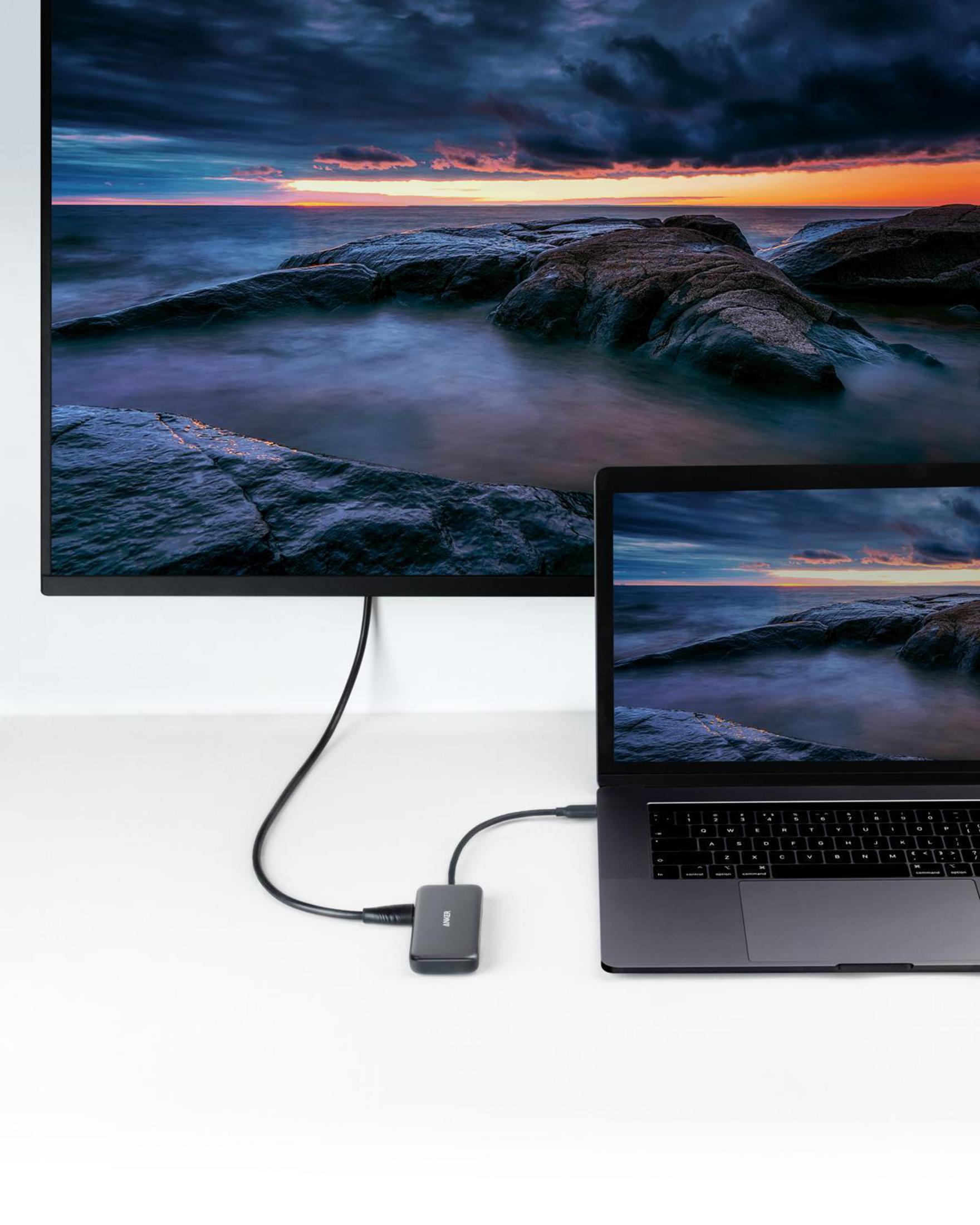 Laptop mit Monitor, der eine Sonnenuntergangsszene zeigt. Dunkles Kabel und Adapter.