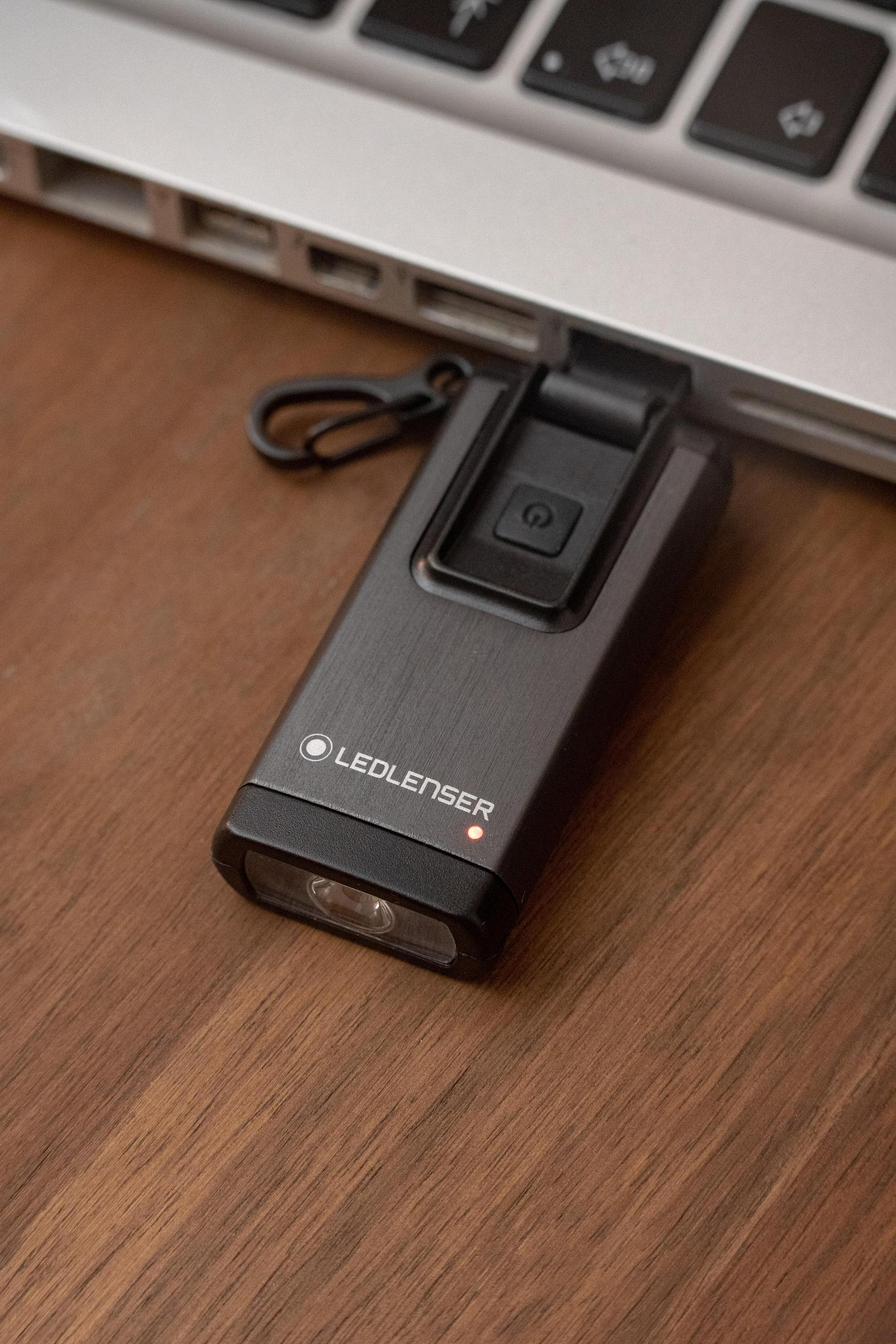 Ciemnoszara latarka LEDLENSER podłączona do laptopa na drewnianym biurku.