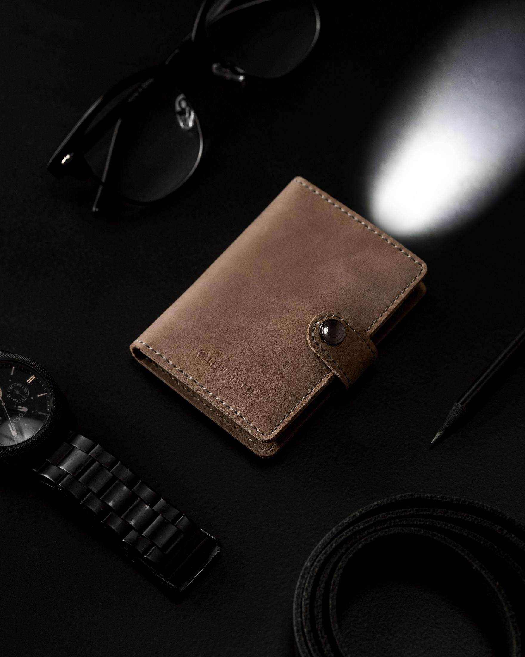 Eine Brieftasche mit einer Taschenlampe wird gezeigt. Auf schwarzem Untergrund mit Uhr und Brille.