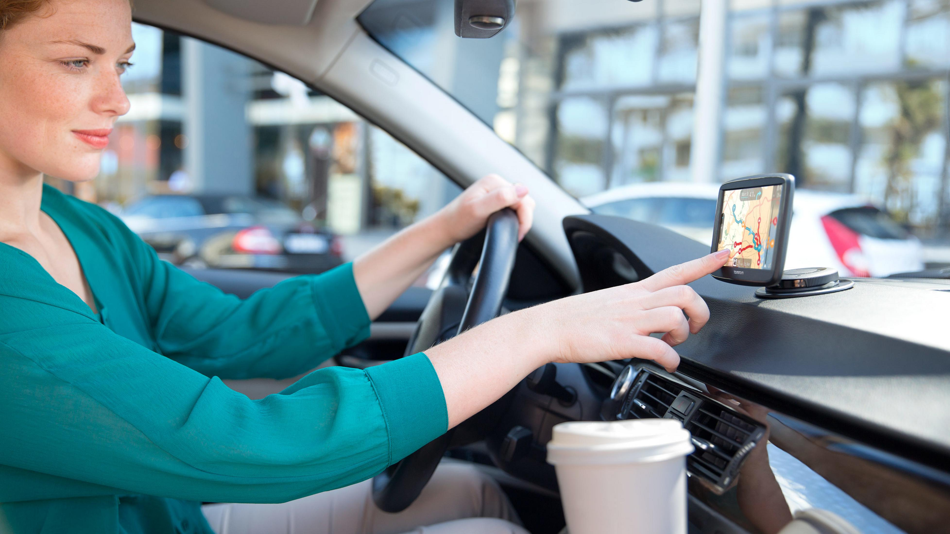 Frau im Auto benutzt GPS. Sie hält das Lenkrad und berührt den Bildschirm. Stadt Hintergrund.