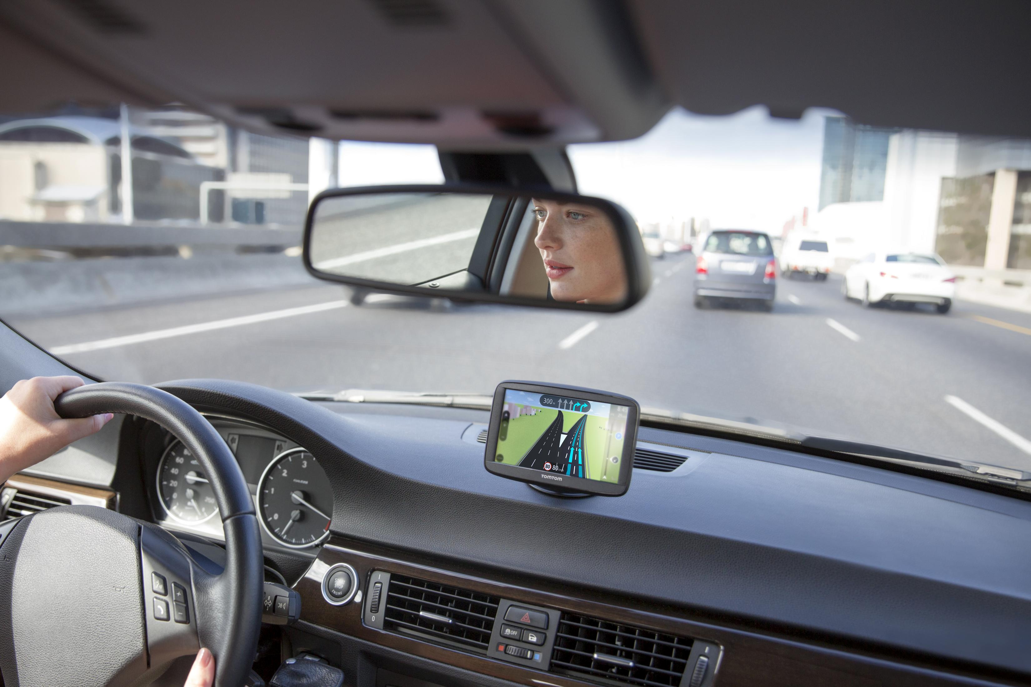 Frau fährt, blickt auf TomTom-Navi auf dem Armaturenbrett. Auto-Innenraum. Autobahn.