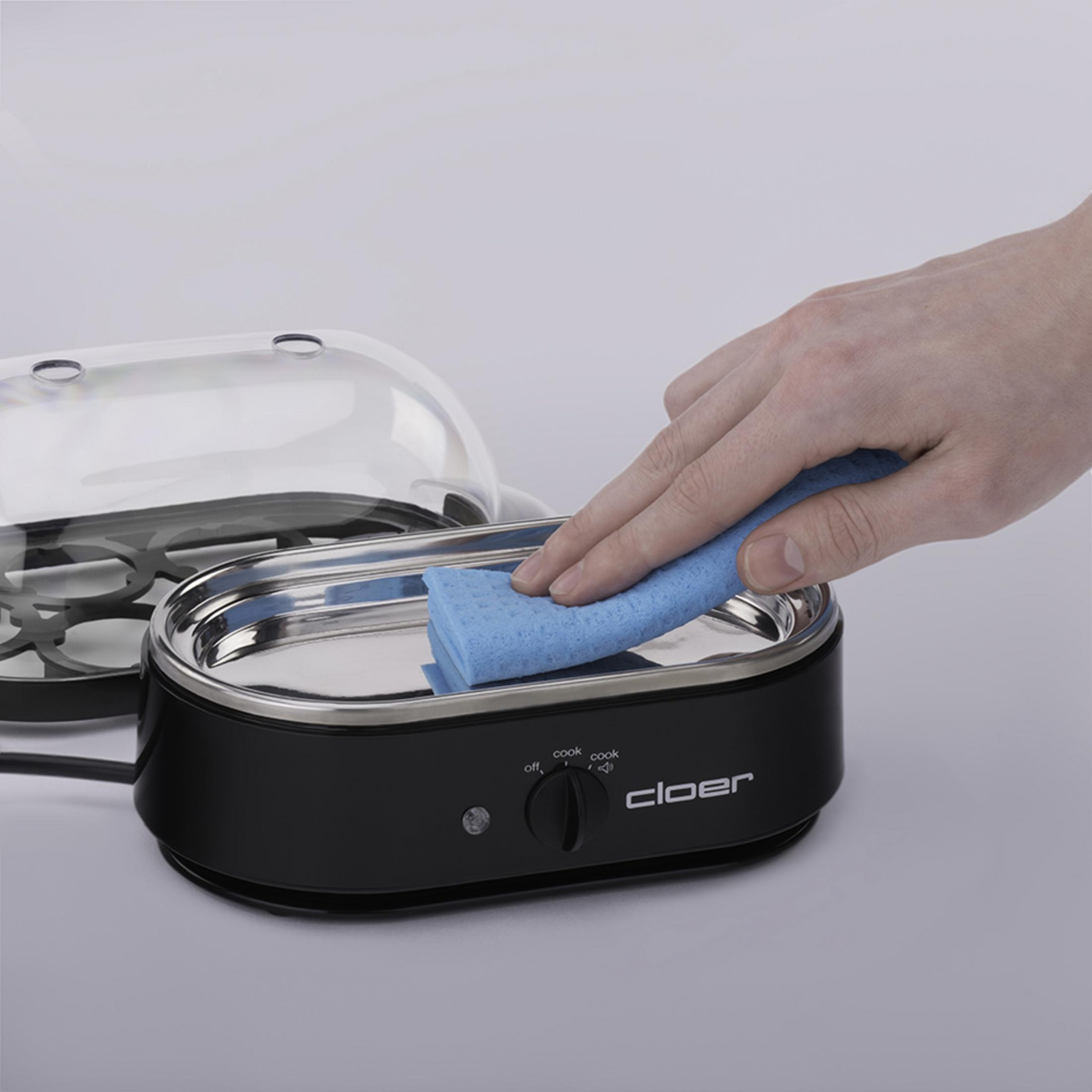 Ręka wyciera wnętrze czarno-srebrnego urządzenia do gotowania jajek niebieską gąbką.