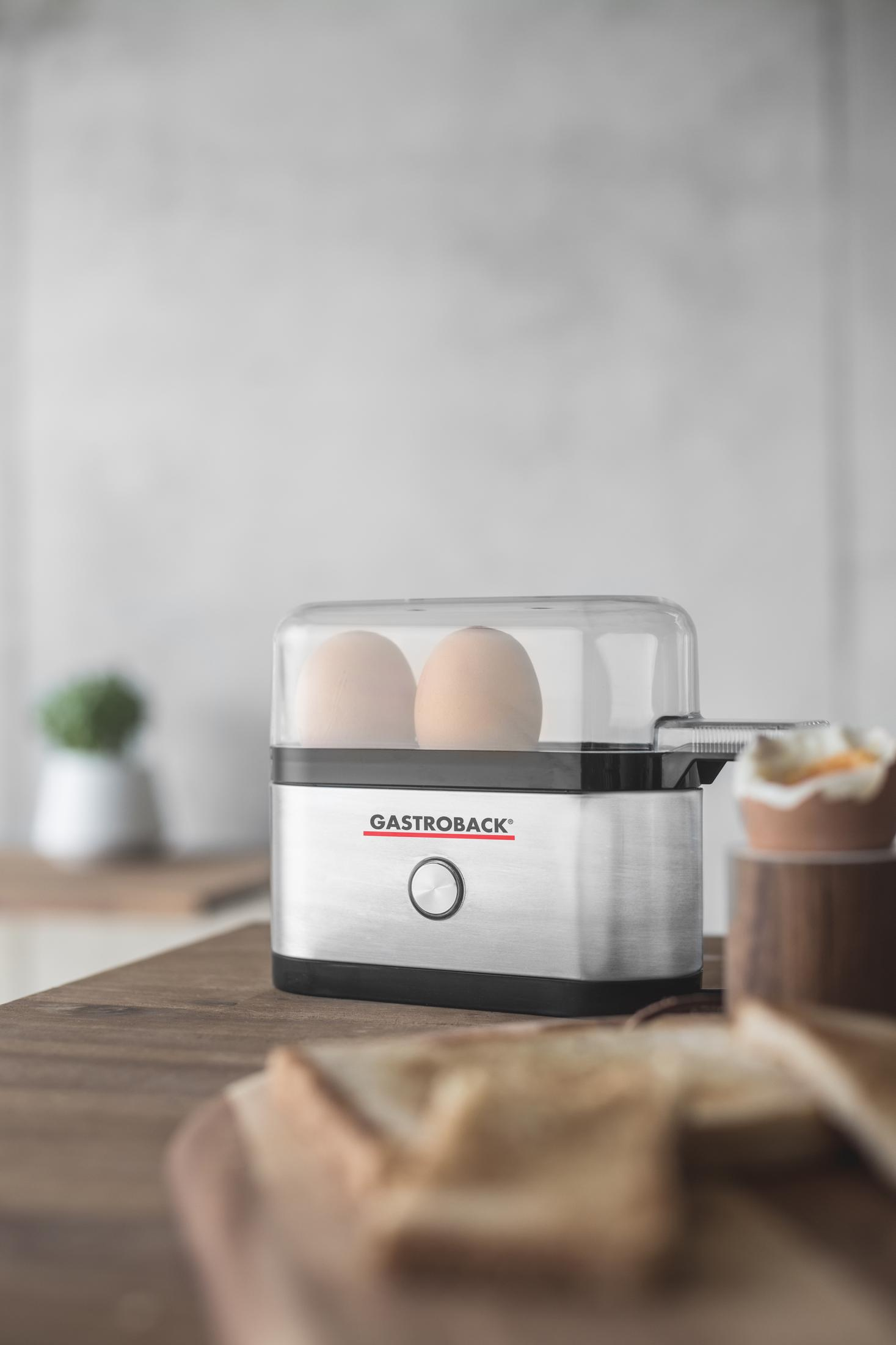 Urządzenie do gotowania jajek z dwoma jajkami w środku. Kromki chleba na pierwszym planie.