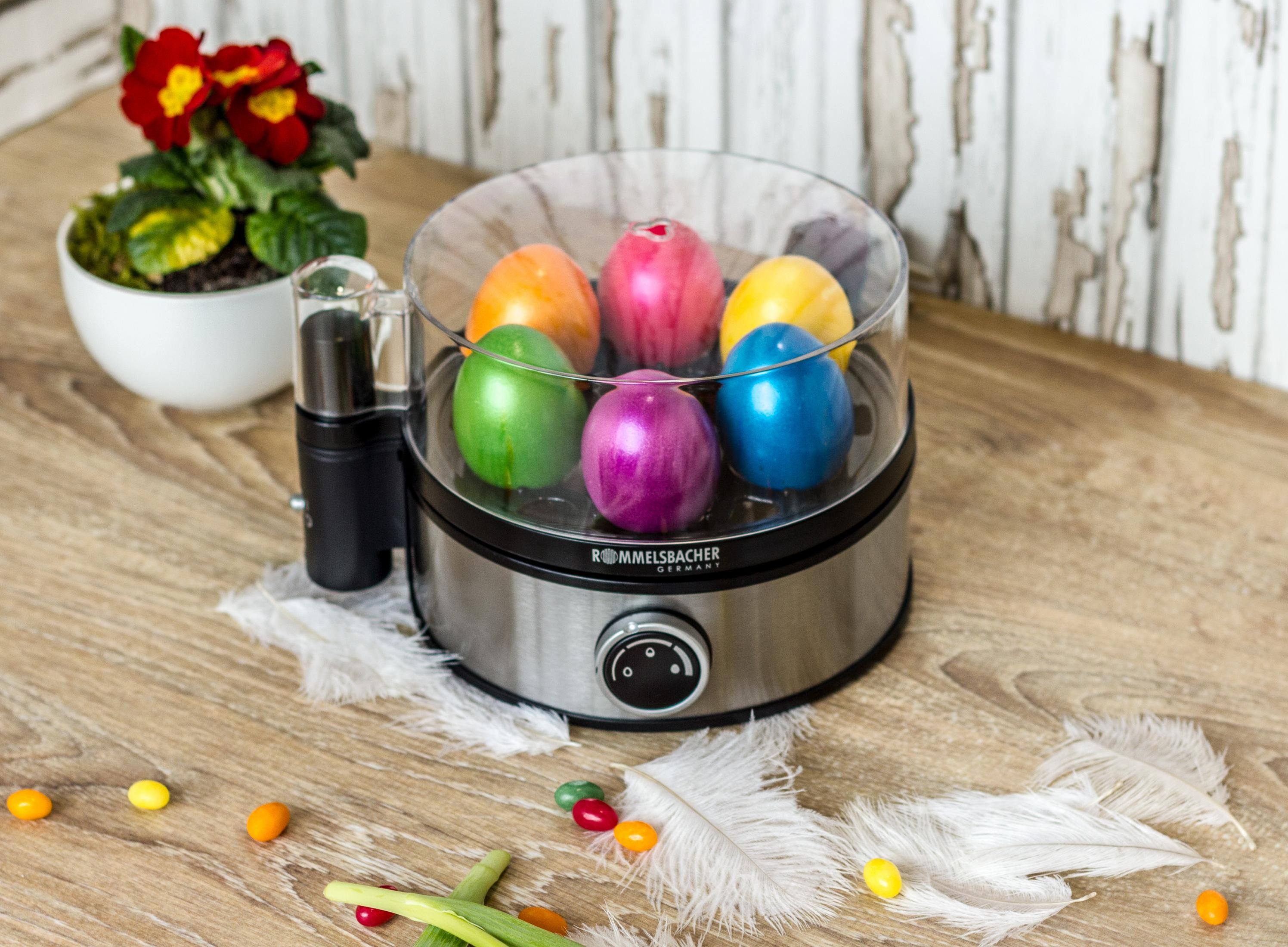 Gotowacz do jajek z kolorowymi jajkami w środku, z doniczką z boku, na drewnianej powierzchni.