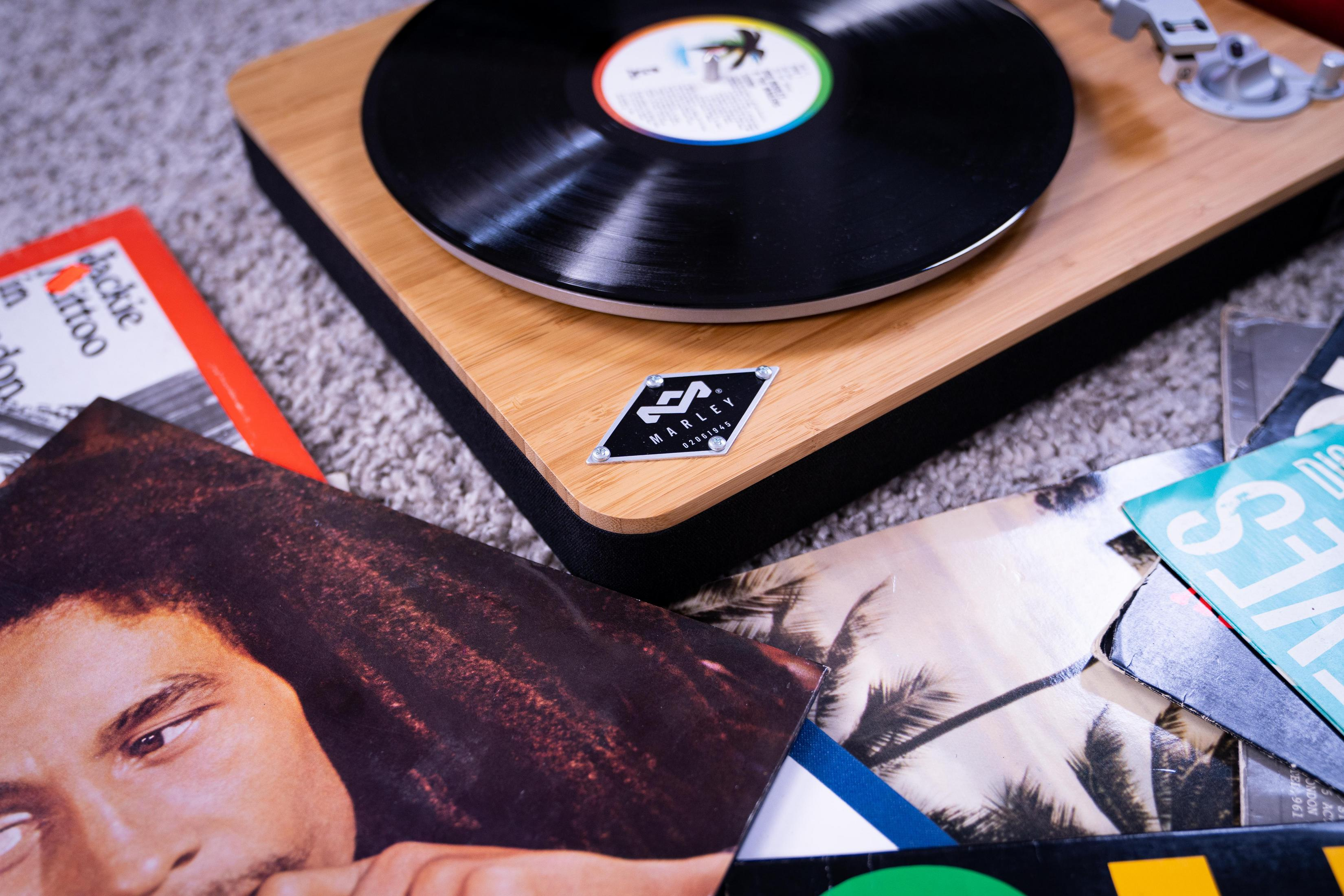 Giradischi con disco in vinile in riproduzione. Copertine di album sparse. Logo Marley visibile.