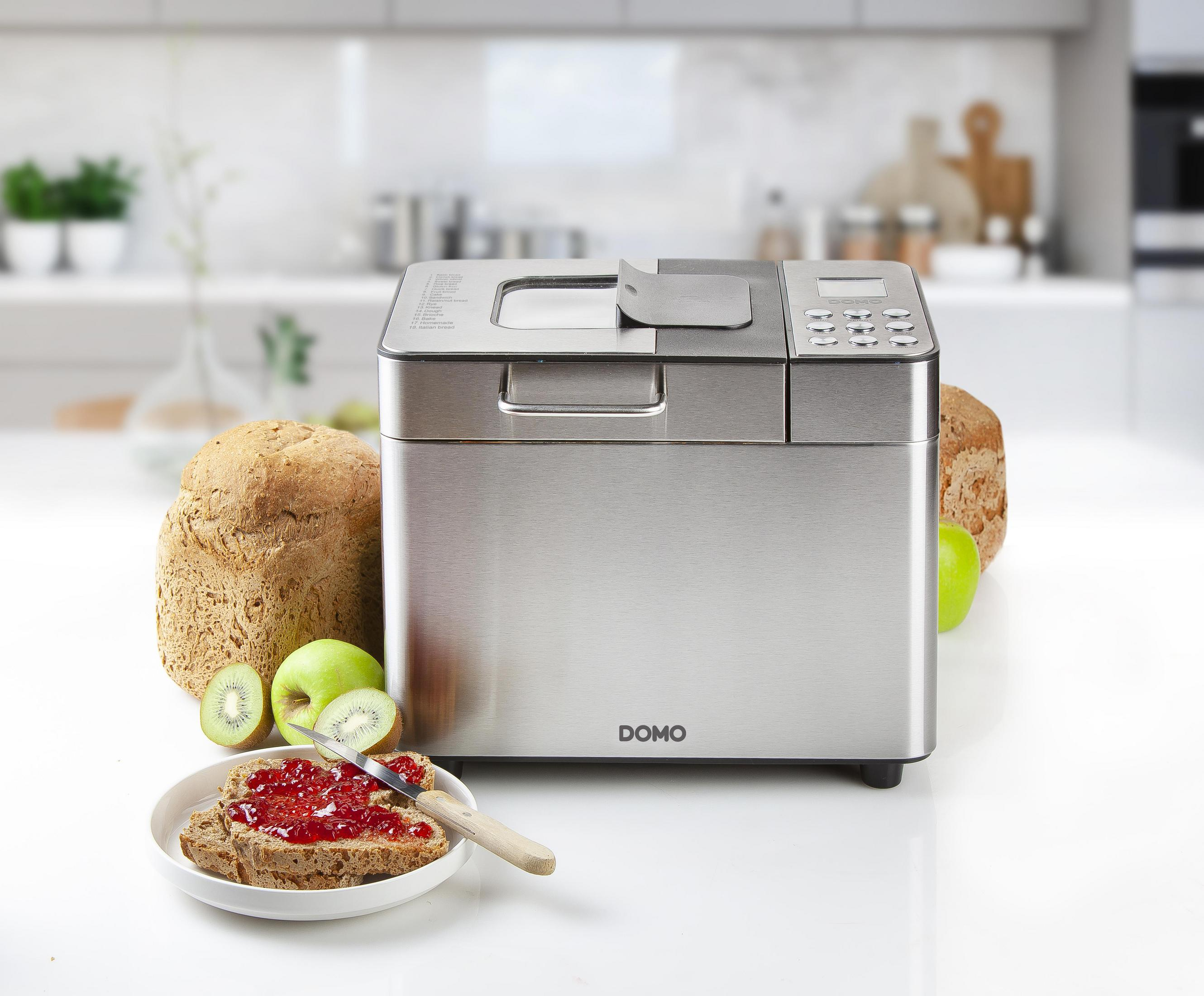 Brotbackmaschine mit Brot und Obst. Brotscheibe mit Marmelade und Messer auf einem Teller.