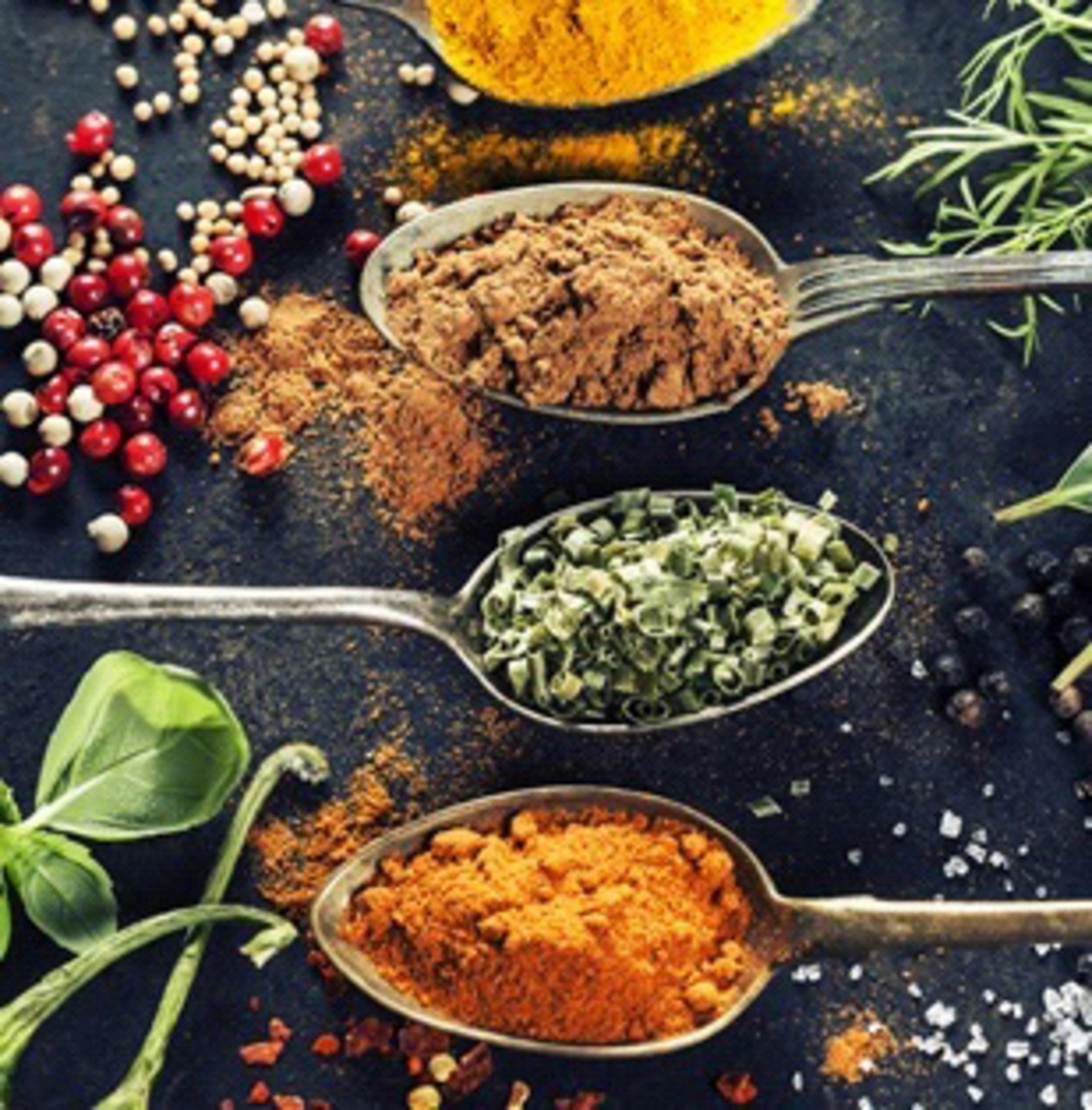 Diverses épices dans des cuillères sur une surface sombre. Les épices incluent du poivre rouge, des herbes.