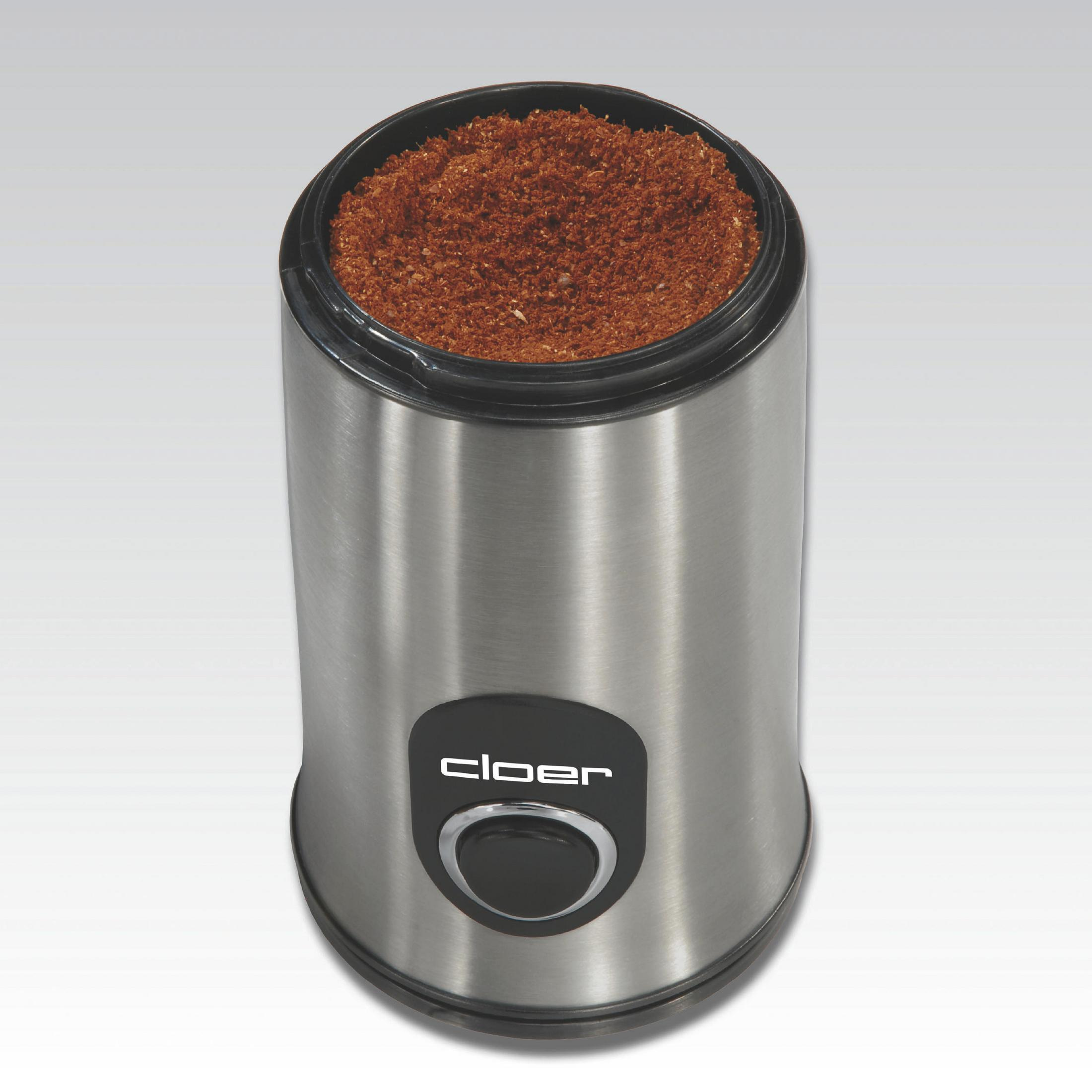 Kaffeemühle mit silbernem Gehäuse, schwarzem Deckel und Kaffeepulver. Weißer Hintergrund.