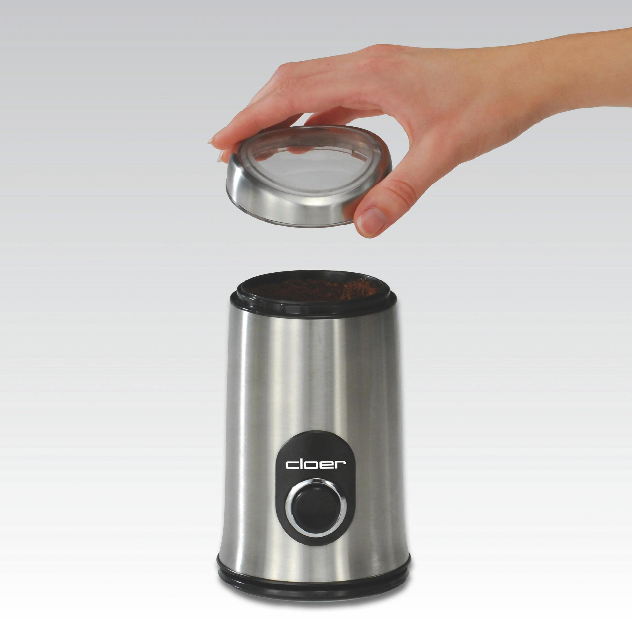 Eine silberne Kaffeemühle mit schwarzem Deckel und eine Hand, die den Deckel abnimmt.