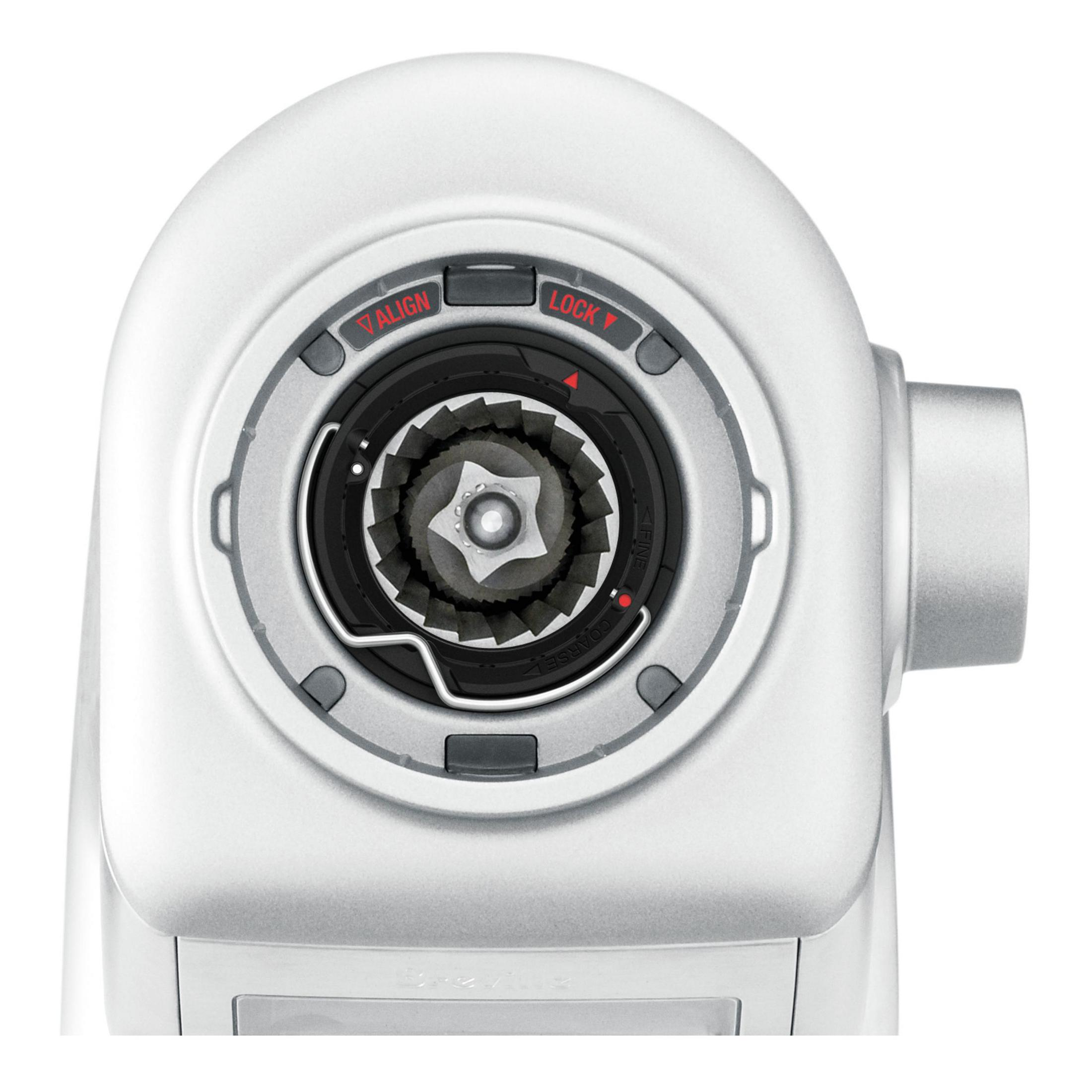 Zbliżenie na młynek do kawy, pokazujące mechanizm mielenia. Młynek ma srebrne wykończenie i ustawienia.