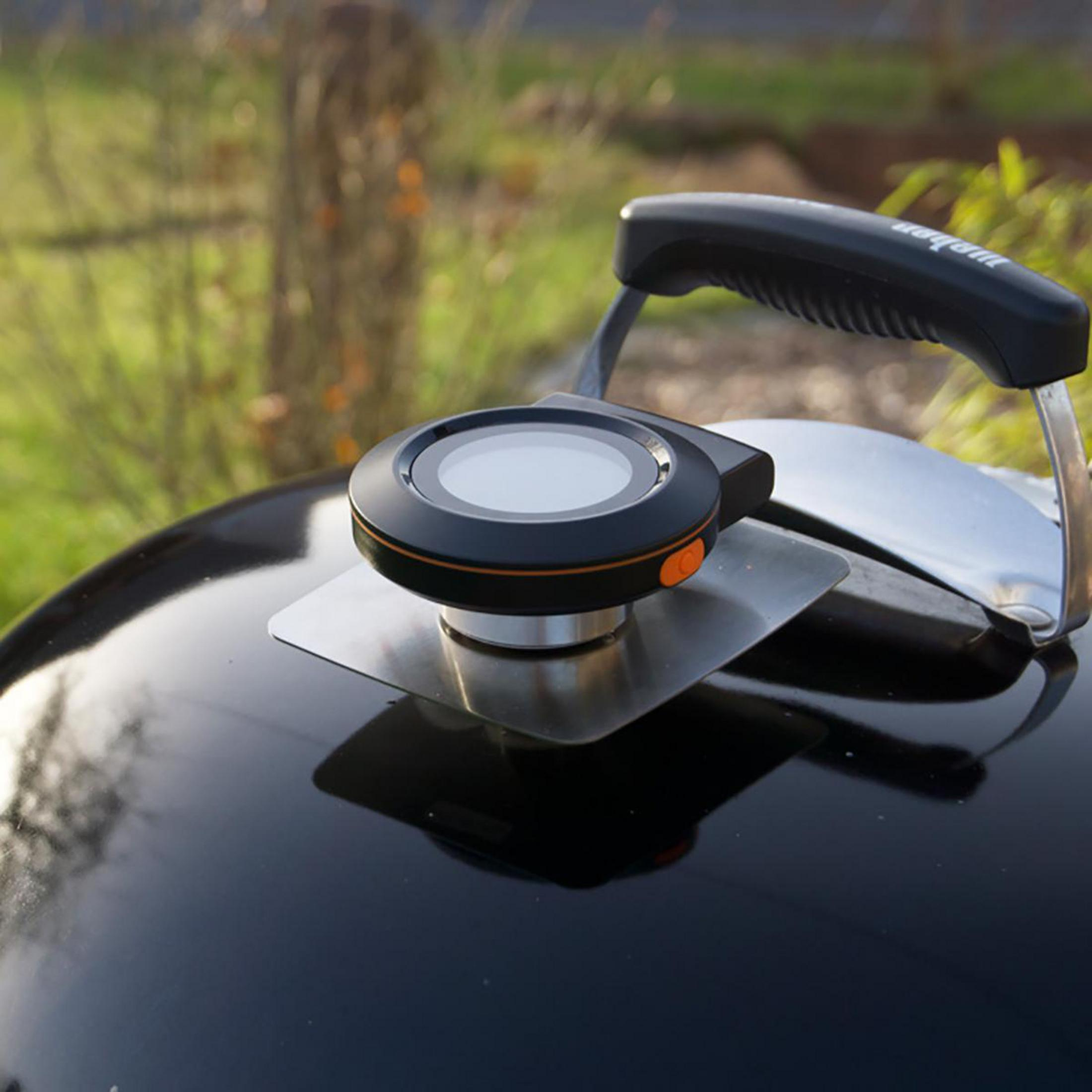 Schwarzes Grillthermometer auf einem Grill. Es befindet sich auf einer weißen Oberfläche.