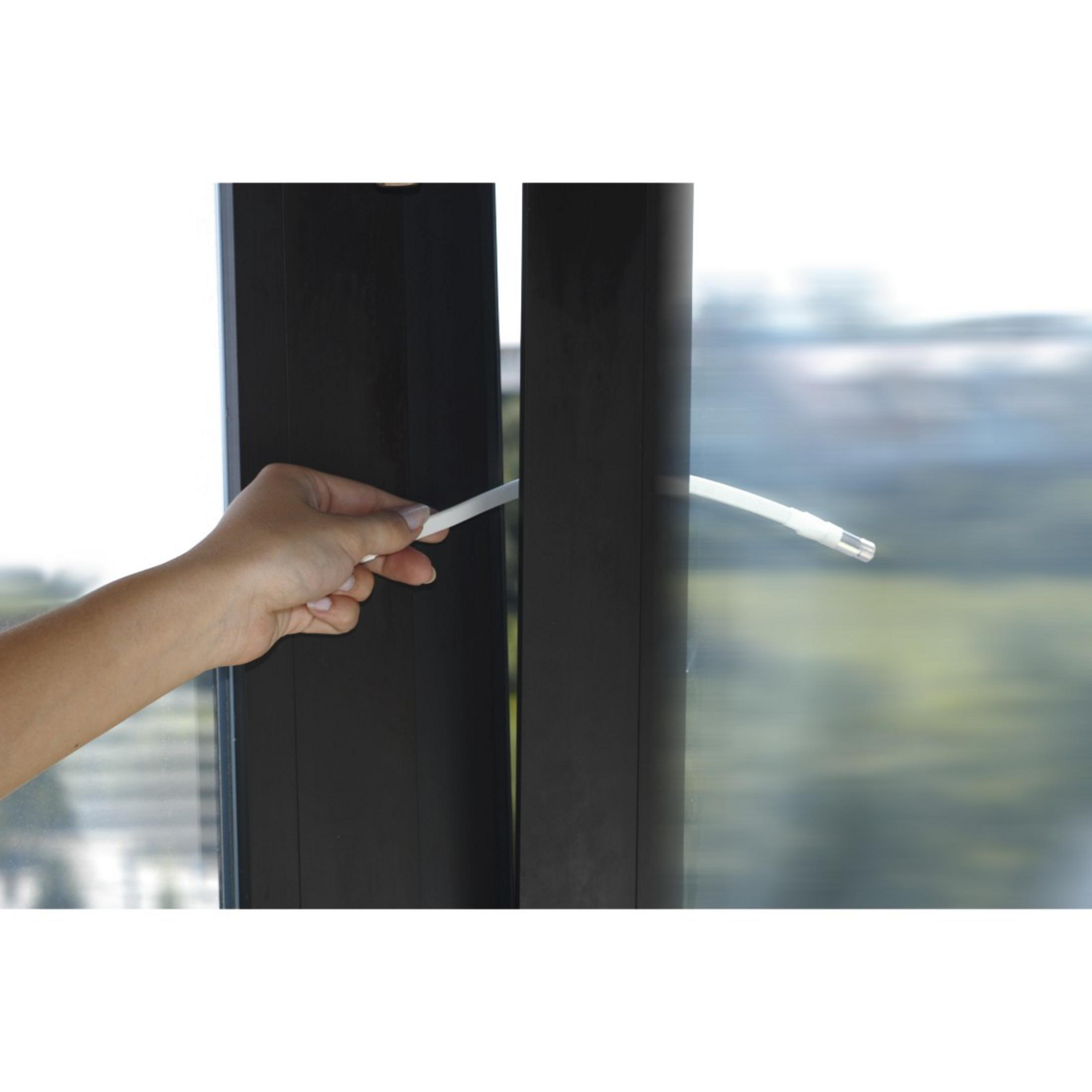Dłoń wkładająca białą, cienką uszczelkę w bok czarnej ramy okiennej.