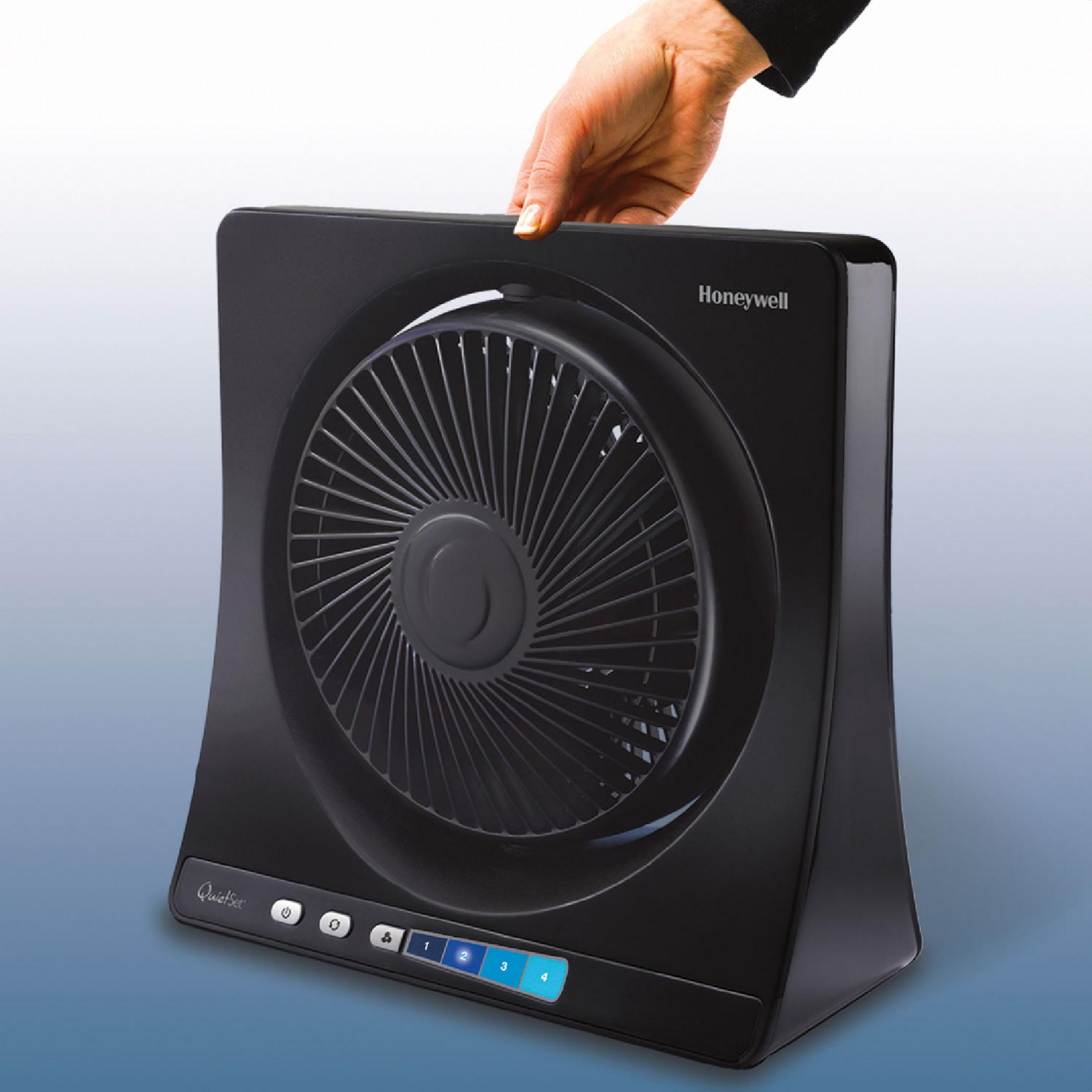 Ventilador de aire negro, una mano sujetando la parte superior. Logotipo de Honeywell y botones de control.
