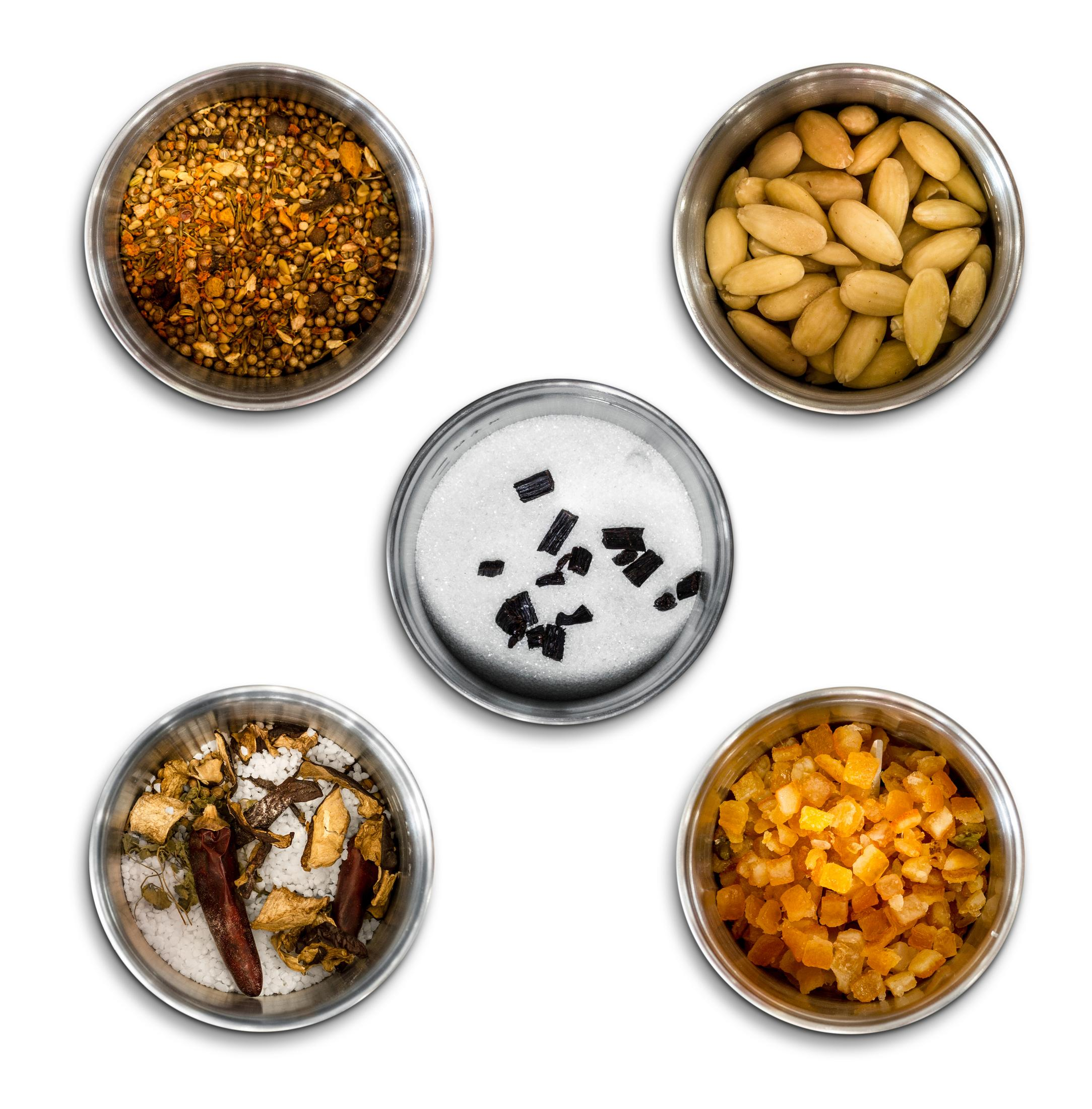 Pięć misek ze składnikami: przyprawy, migdały, cukier z czarnymi kawałkami, suszone składniki i skórka pomarańczowa.