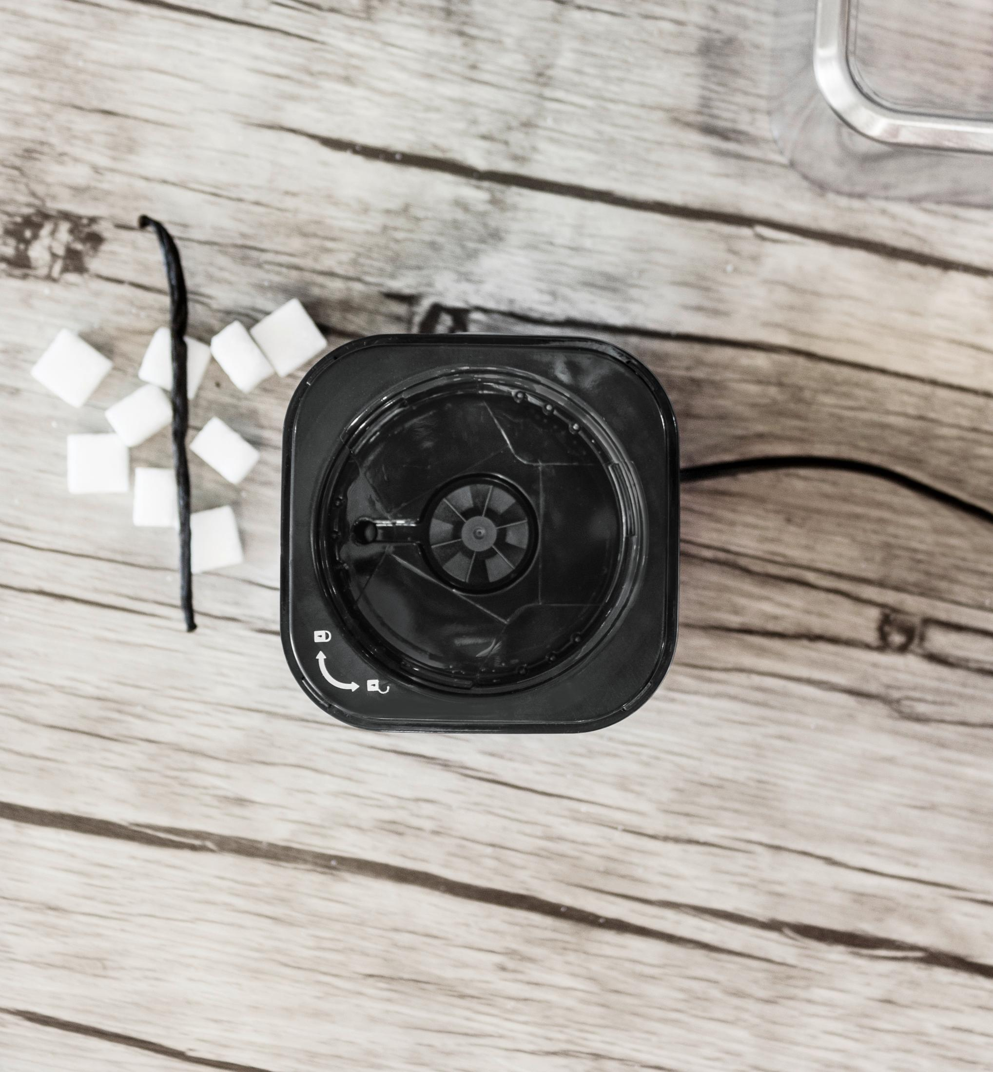 Widok z góry na pokrywę młynka do kawy, kostki cukru i laskę wanilii na drewnie.