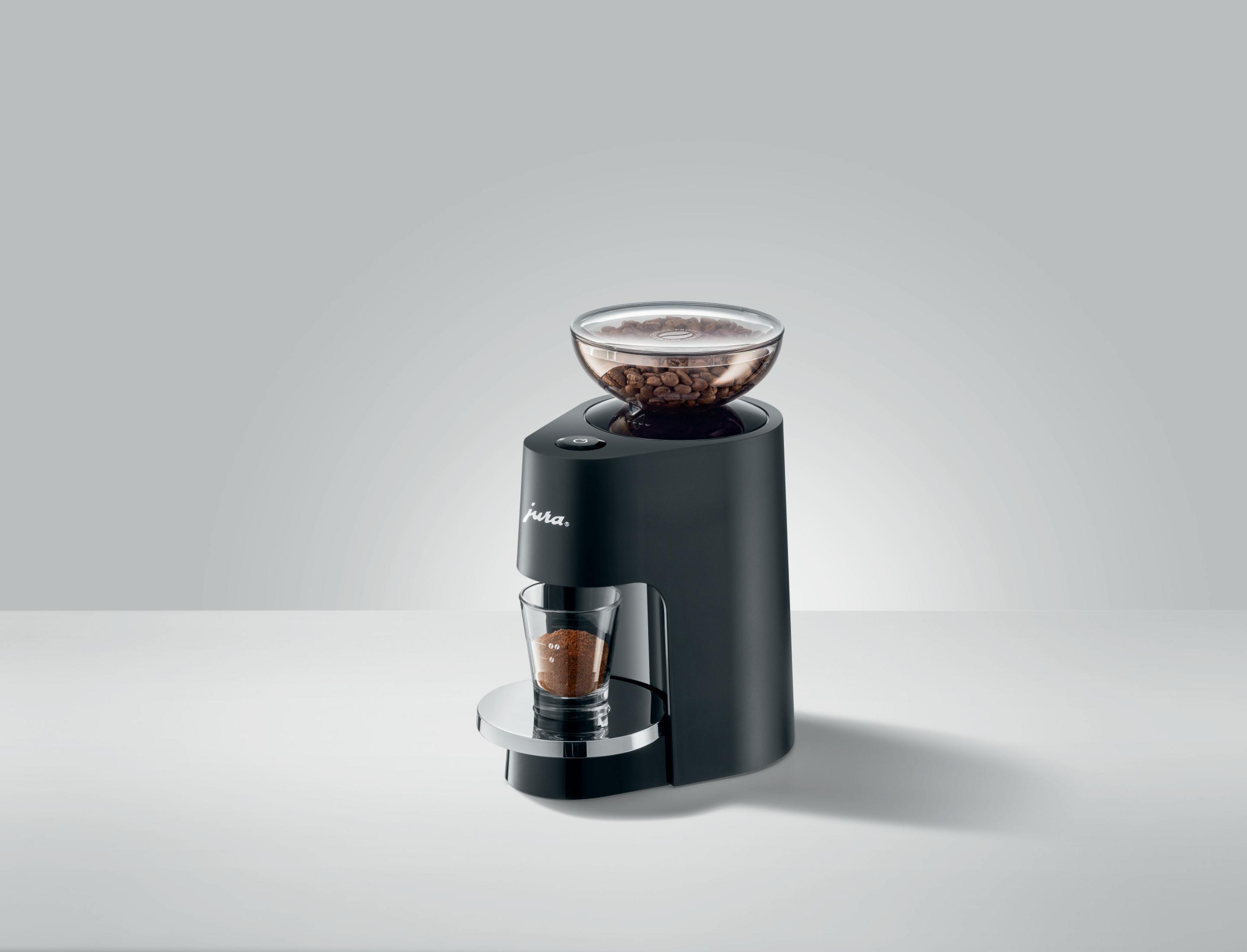 Schwarze Kaffeemaschine mit Kaffeebohnen in einem transparenten Behälter und einem Glas mit Kaffeepulver.