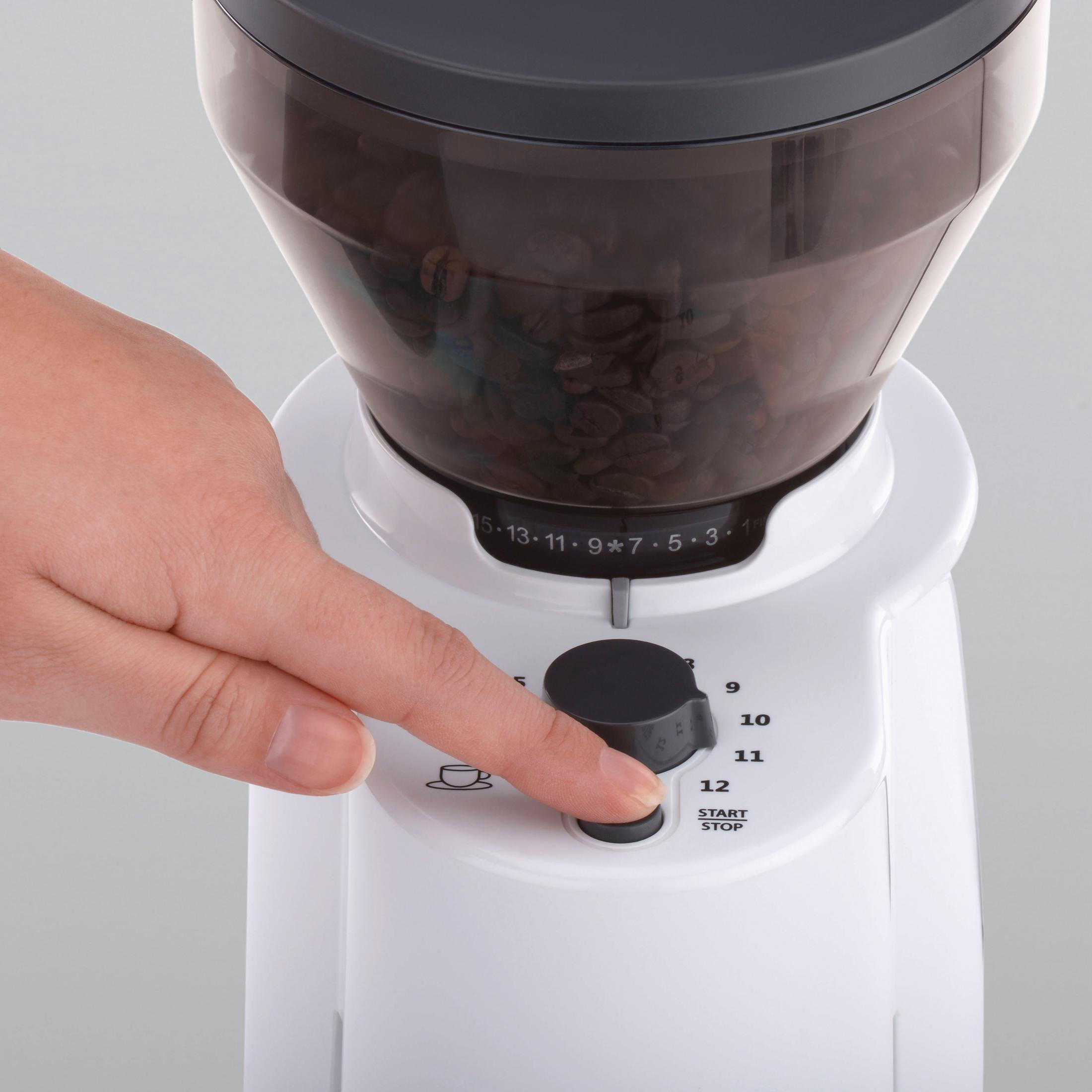 Die Hand einer Person drückt einen Knopf auf einer weißen Kaffeemühle mit Kaffeebohnen im Behälter.