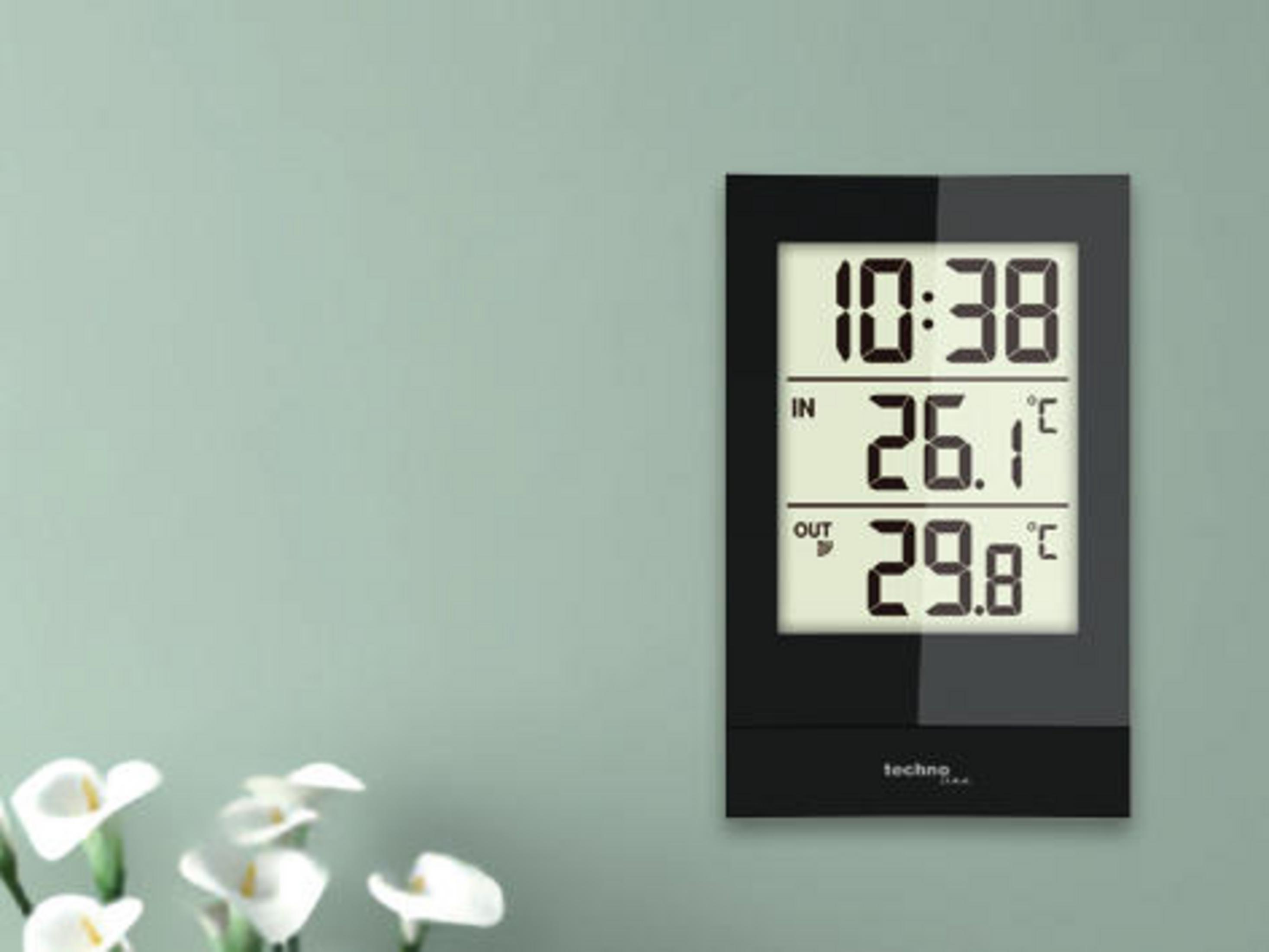 Un termometro digitale in bianco e nero su una parete verde, che mostra l'ora e le temperature.