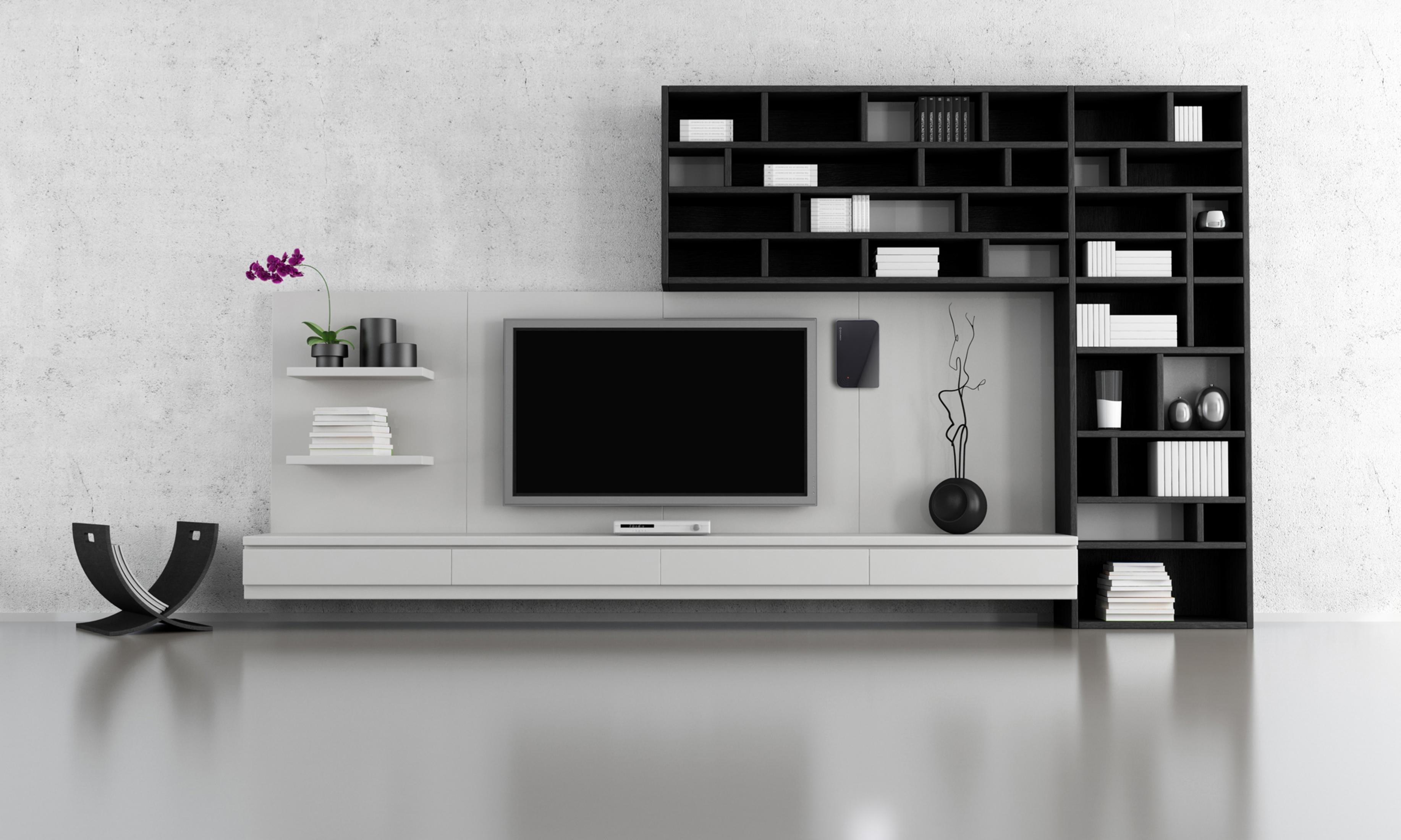 Modernes Wohnzimmer mit TV an der Wand. Bücherregale, Deko. Grauer Boden.