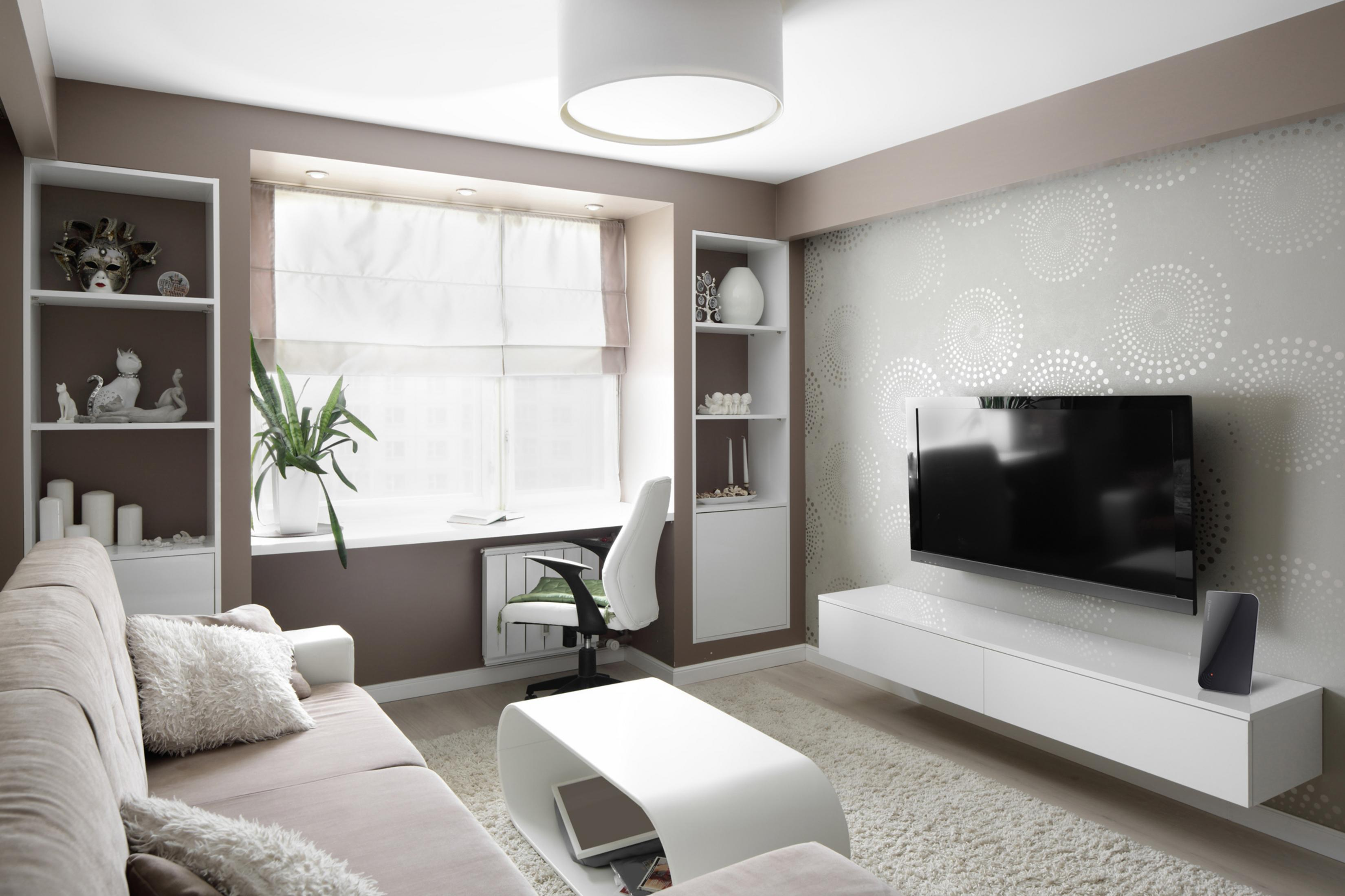 Modernes Wohnzimmer mit beigem Sofa, weißen Regalen und einem großen Fernseher an der Wand.