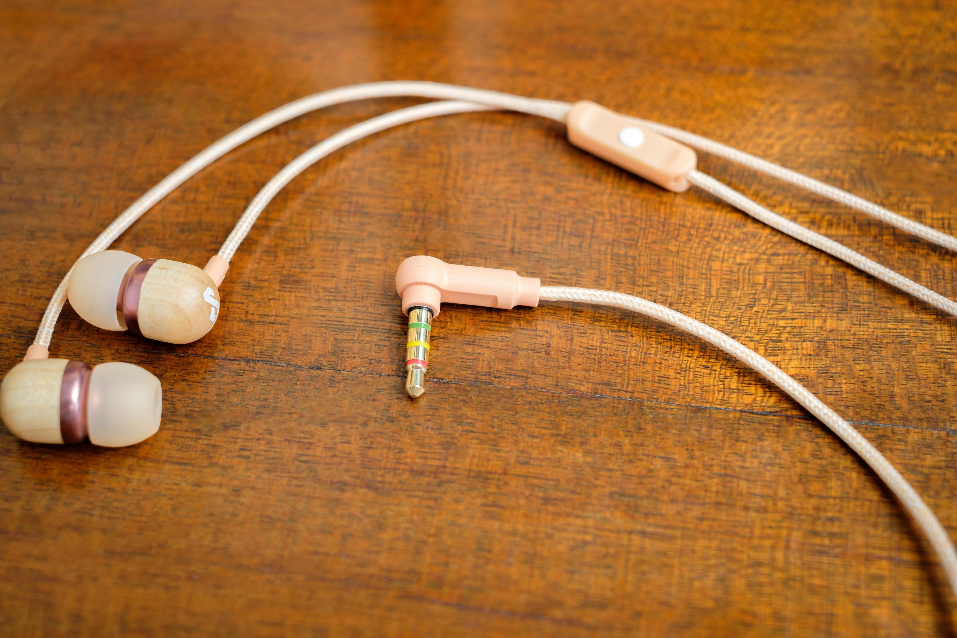 Kopfhörer mit pinkfarbenem Kabel und Stecker. Sie liegen auf einer Holzoberfläche.