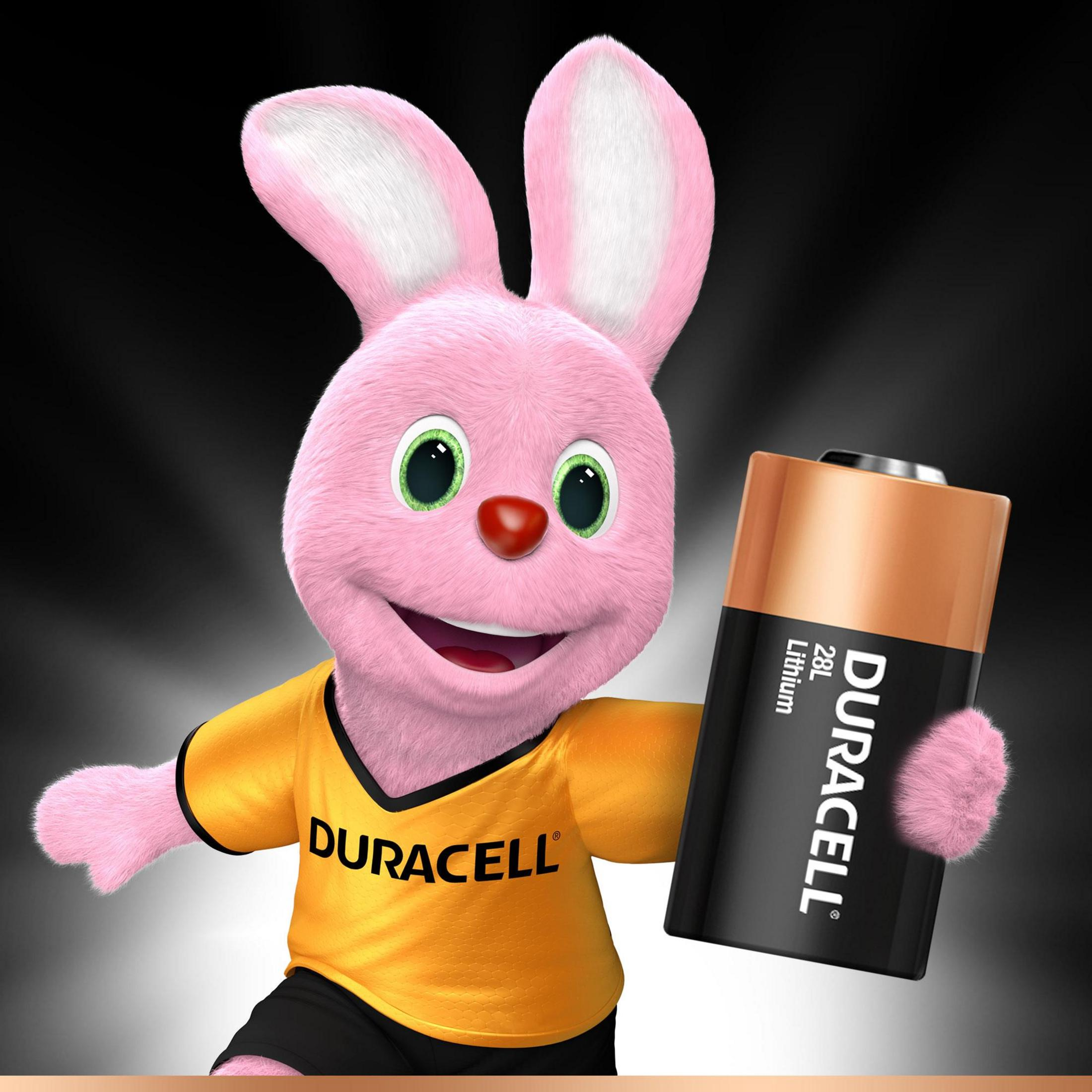 Różowy królik Duracell trzymający baterię Duracell. Żółta koszulka, czarne szorty.