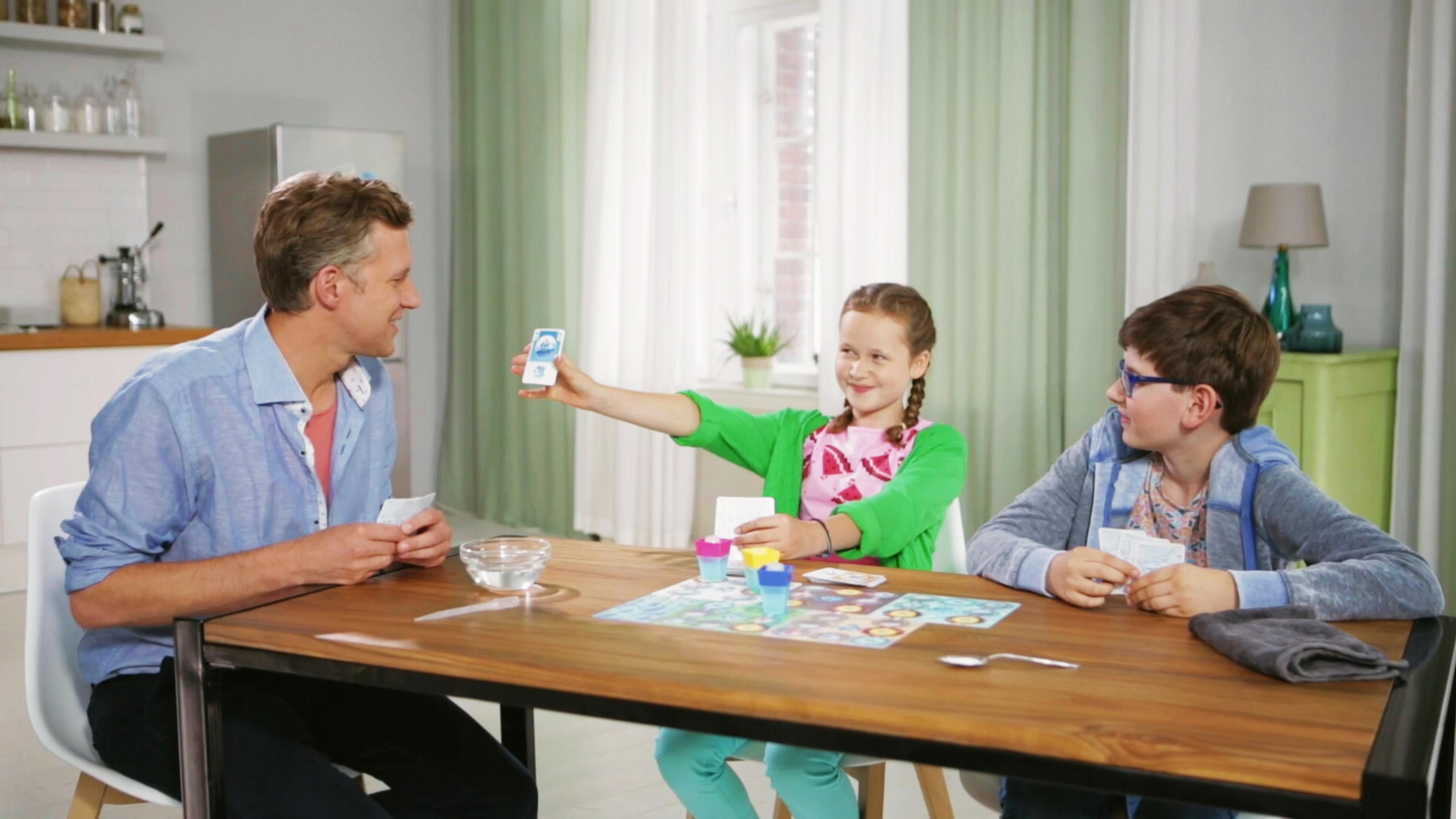 Rodzina gra w grę przy stole. Widoczne karty i elementy gry.