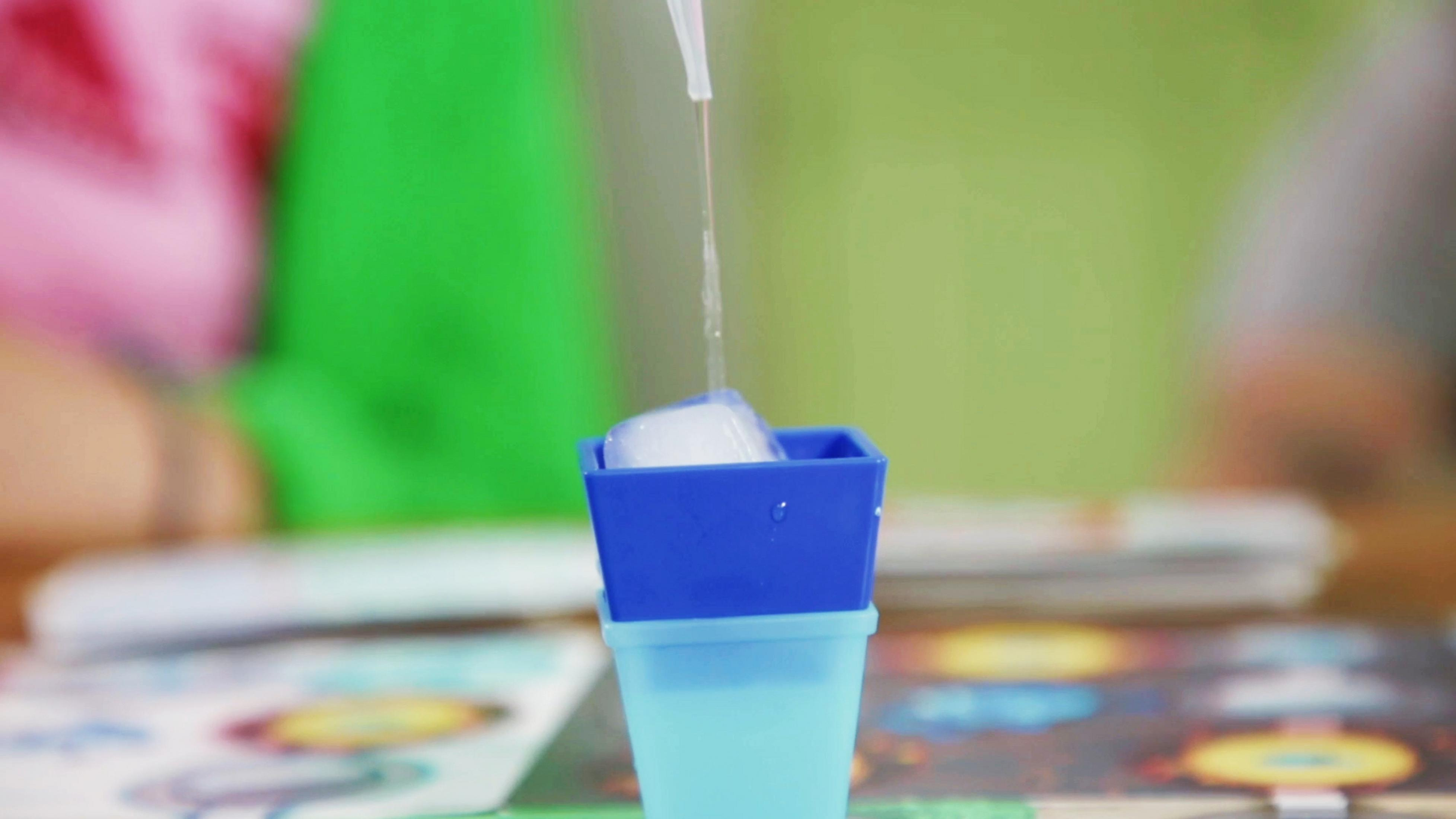 Woda wlewana do małego niebieskiego pojemnika z kostką lodu.