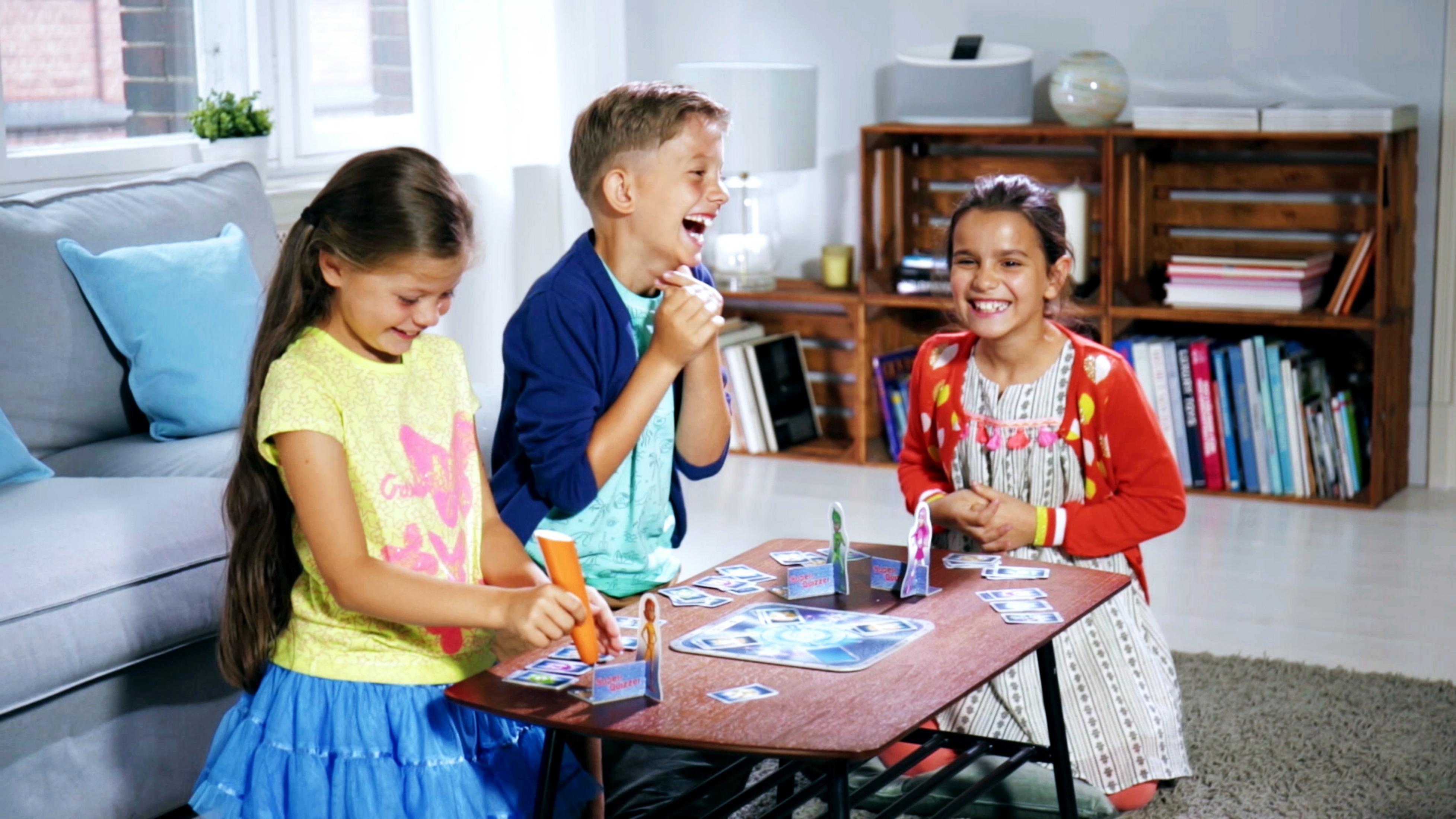 Drei Kinder spielen ein Spiel. Sie lächeln und lachen an einem Tisch mit Karten.