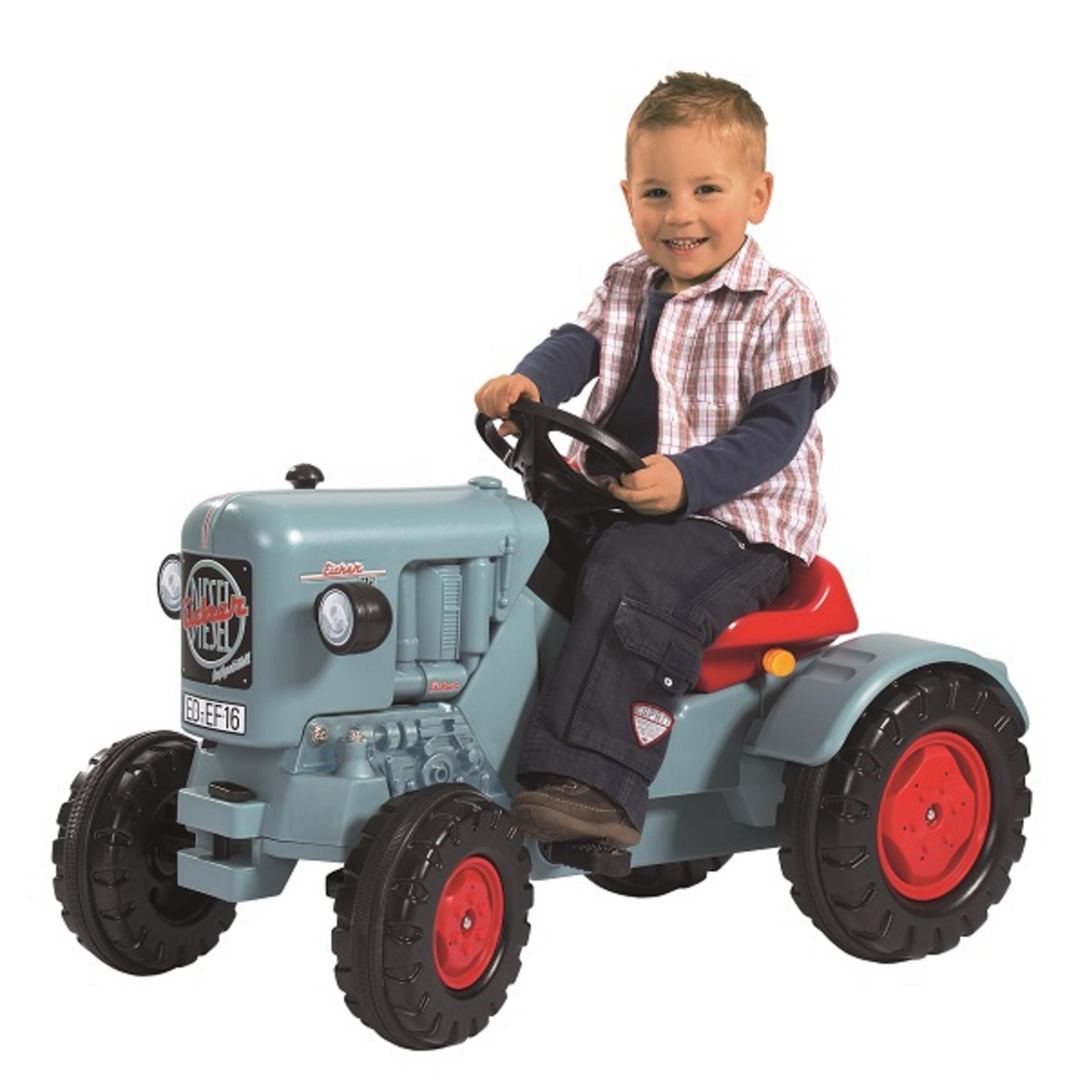 Ein kleiner Junge fährt auf einem blau-grauen Spielzeugtraktor mit roten Rädern und lächelt.