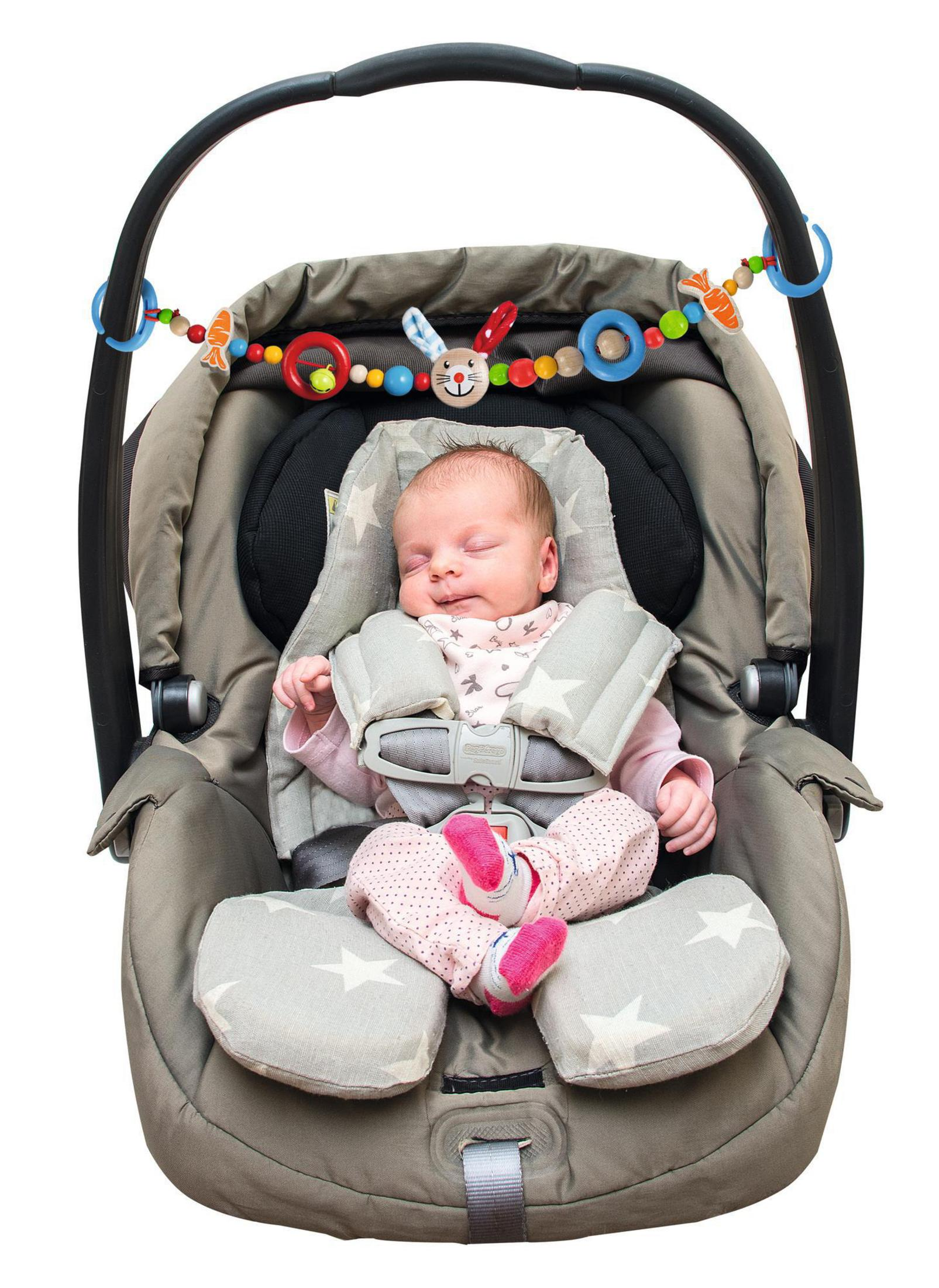 Baby schläft im Autositz. Rosa Outfit, Sternmuster. Spielzeugbogen darüber.