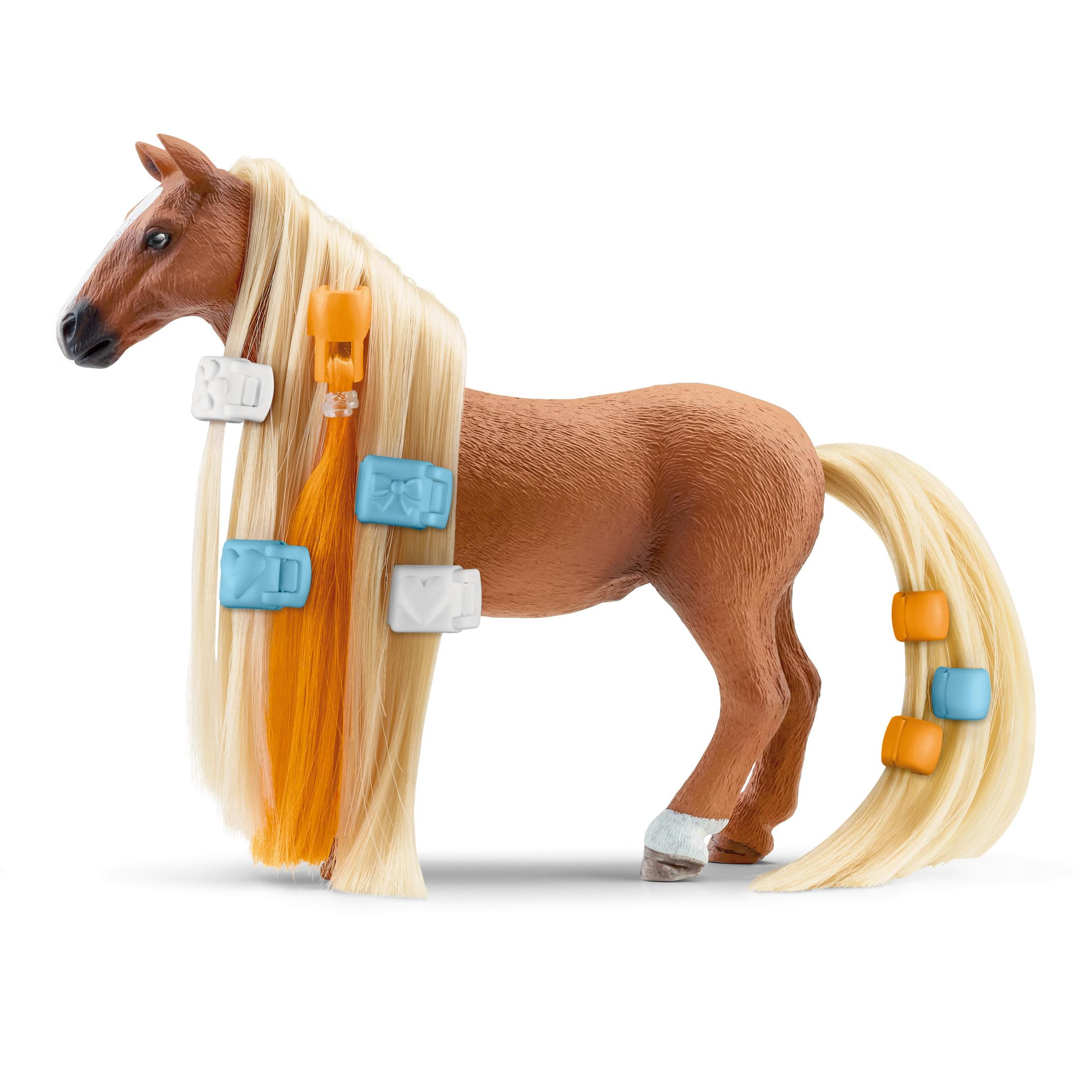 Ein braunes Spielzeugpferd mit blondem Mähne und Schweif, verziert mit bunten Clips, steht auf weißem Untergrund.