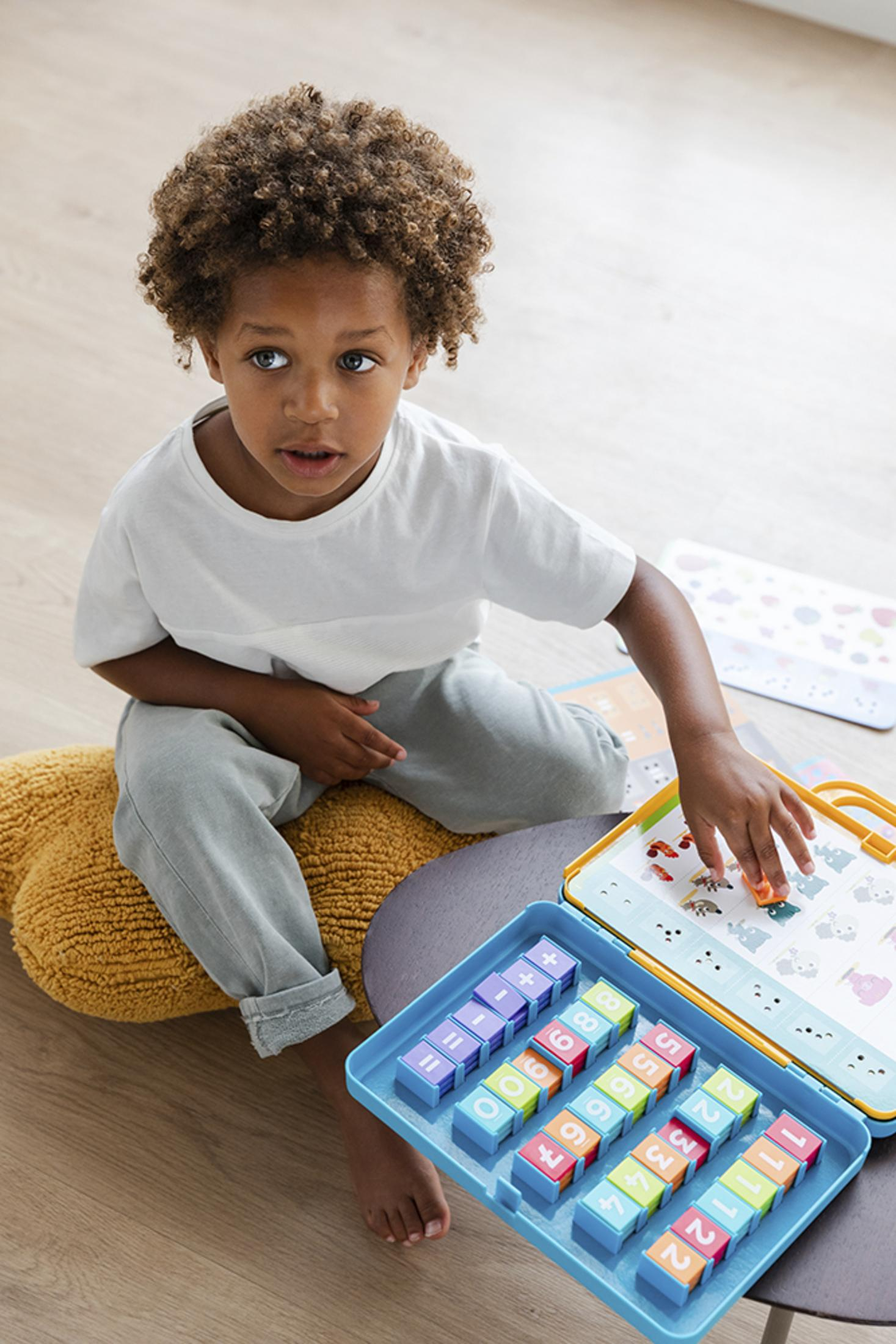 Ein kleiner Junge spielt mit bunten Blöcken und einem Spielzeug, sitzt auf einem Hocker.