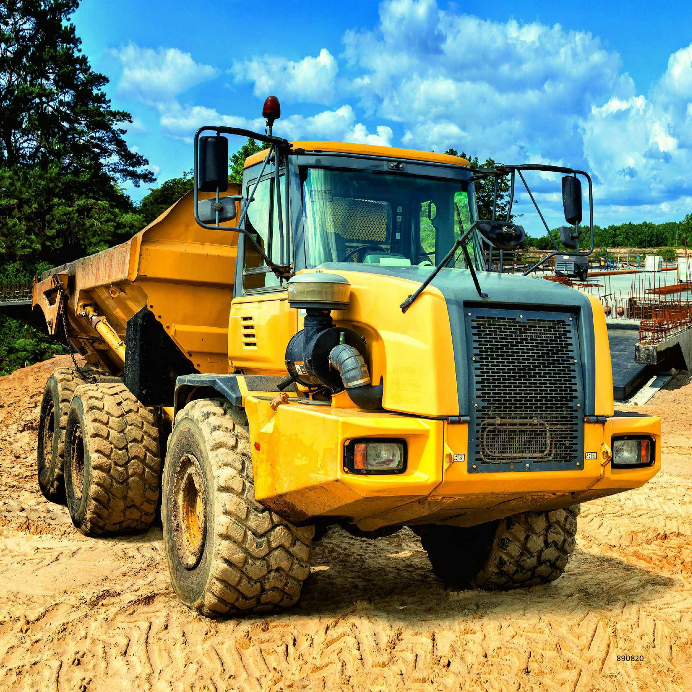 Żółta ciężarówka budowlana na piasku z niebieskim tłem nieba.