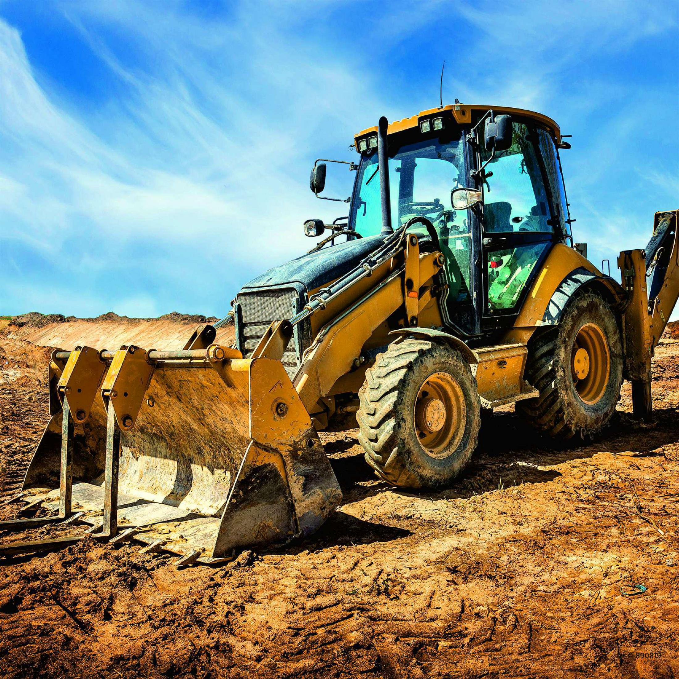 Żółta koparka na ziemi pod niebieskim niebem z chmurami. Łyżka jest opuszczona.