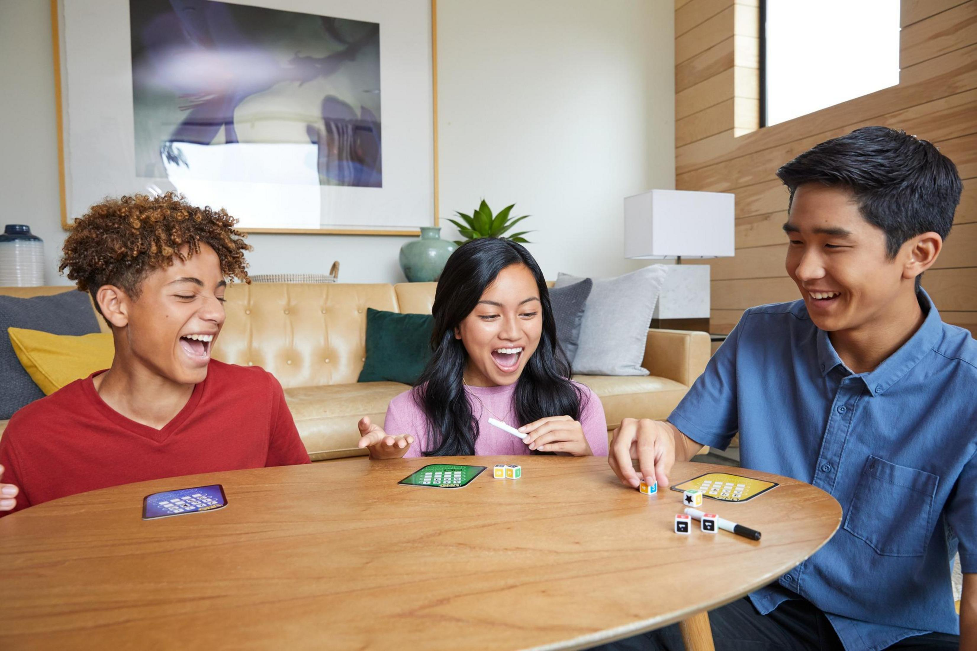 Drei Personen spielen ein Brettspiel. Sie lachen und schauen auf das Spielbrett.