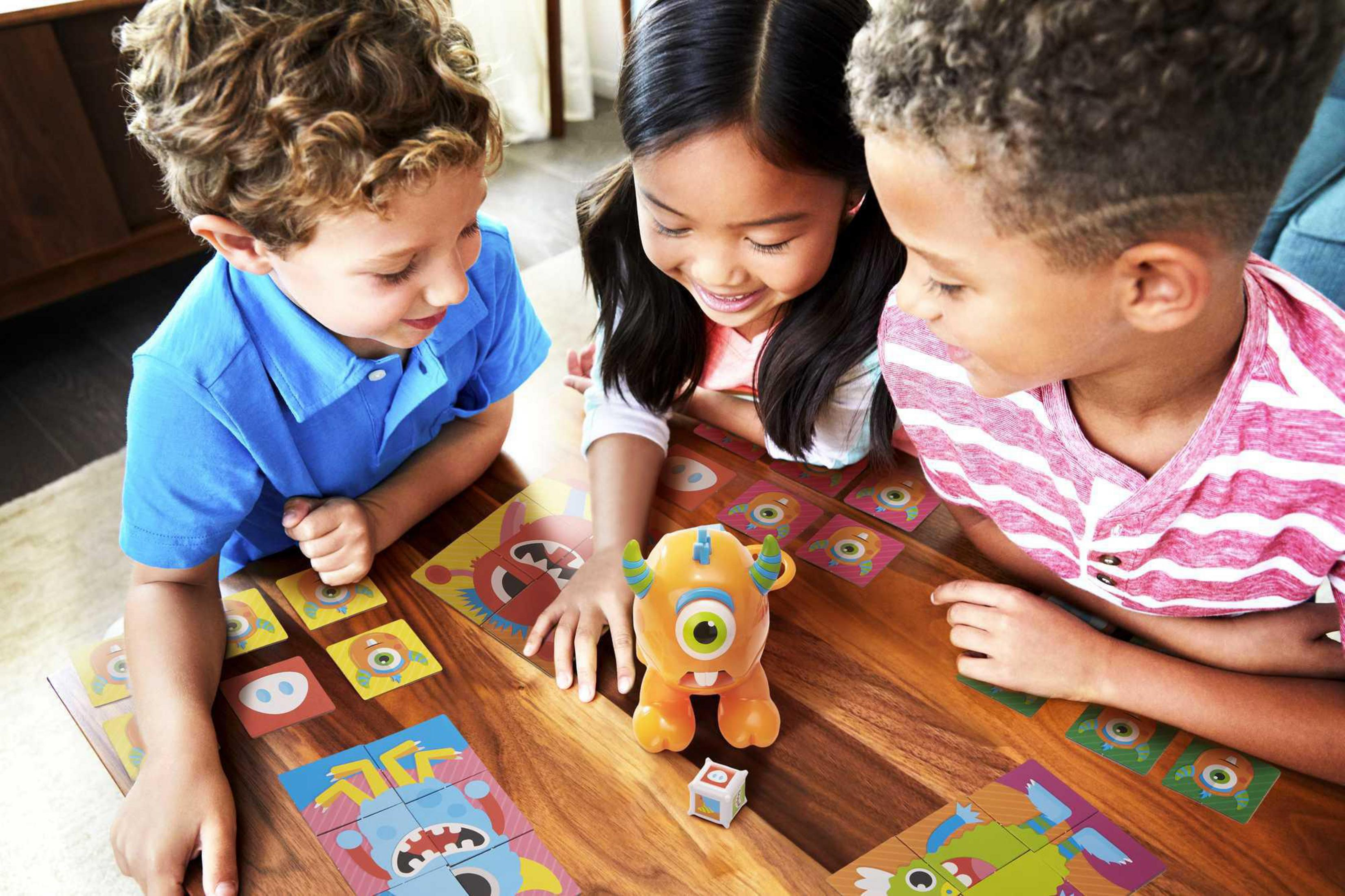 Drei Kinder spielen ein Brettspiel. Monster und Karten liegen auf dem Tisch.