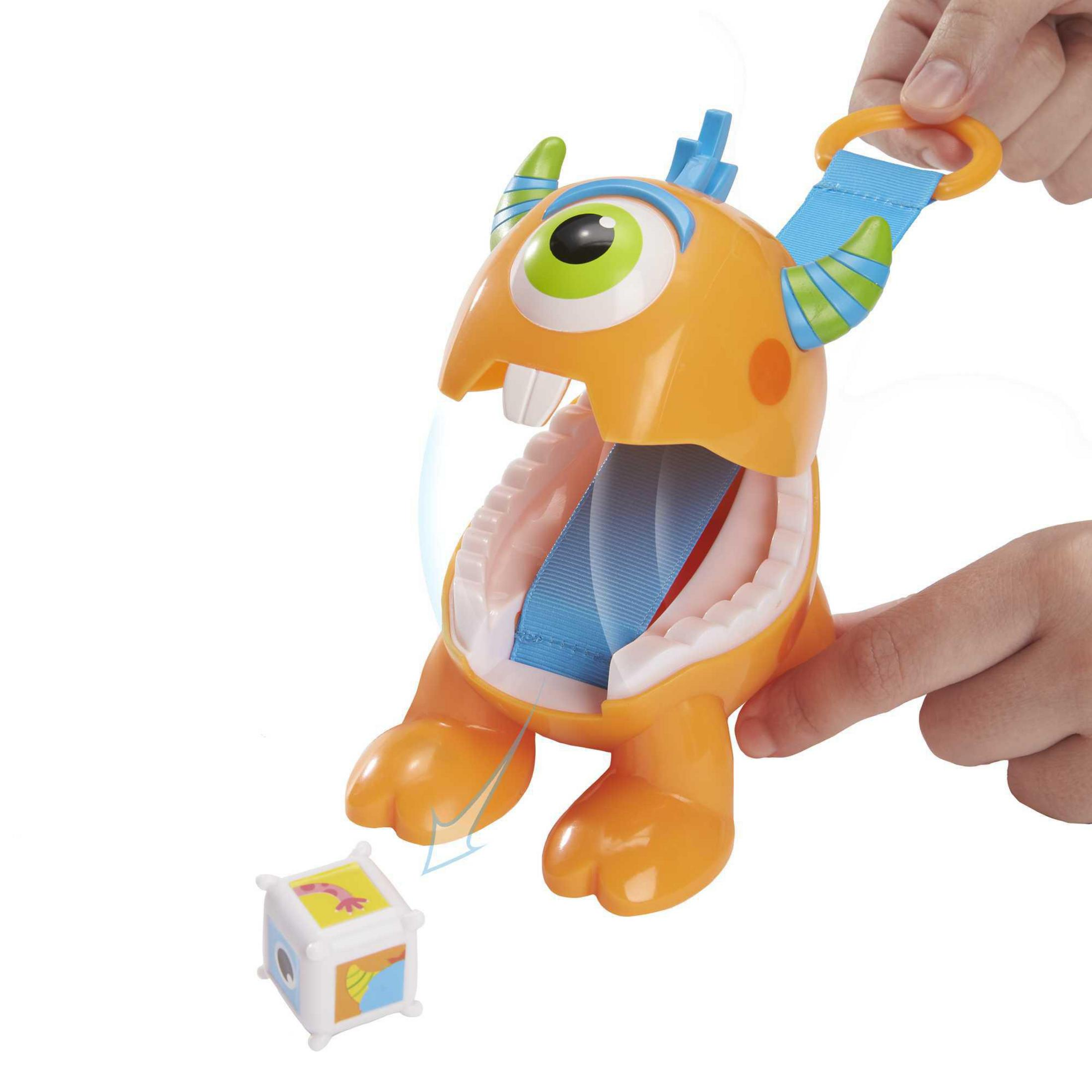 Orangenes Monstermonsterspielzeug mit einem Würfel davor, das von Händen bedient wird, auf weißem Hintergrund.